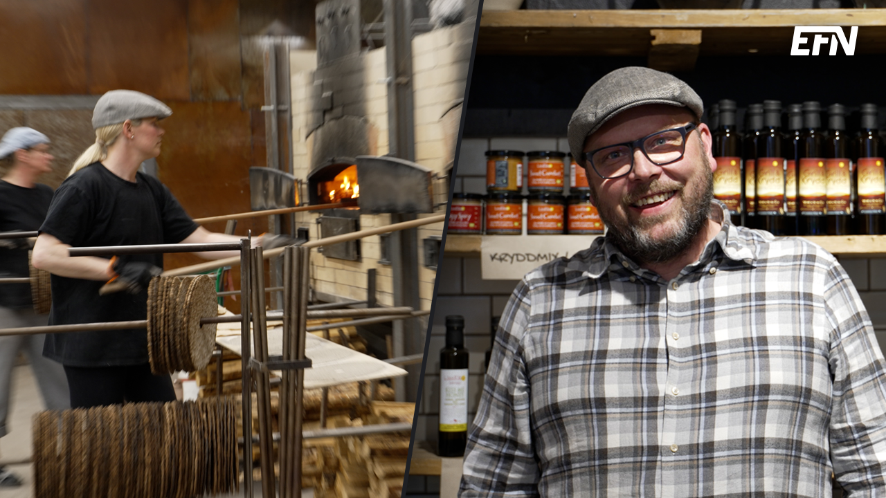 Anders Åkerberg står och ler framför kameran. I bakgrunden bakas det knäckebröd i fabriken. 
