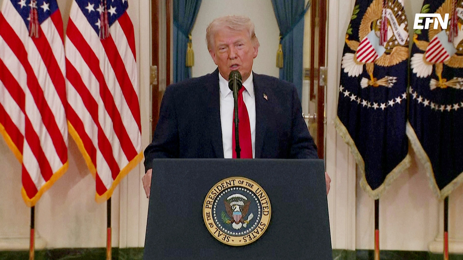 Man vid presidentpodium med amerikanska flaggor i bakgrunden