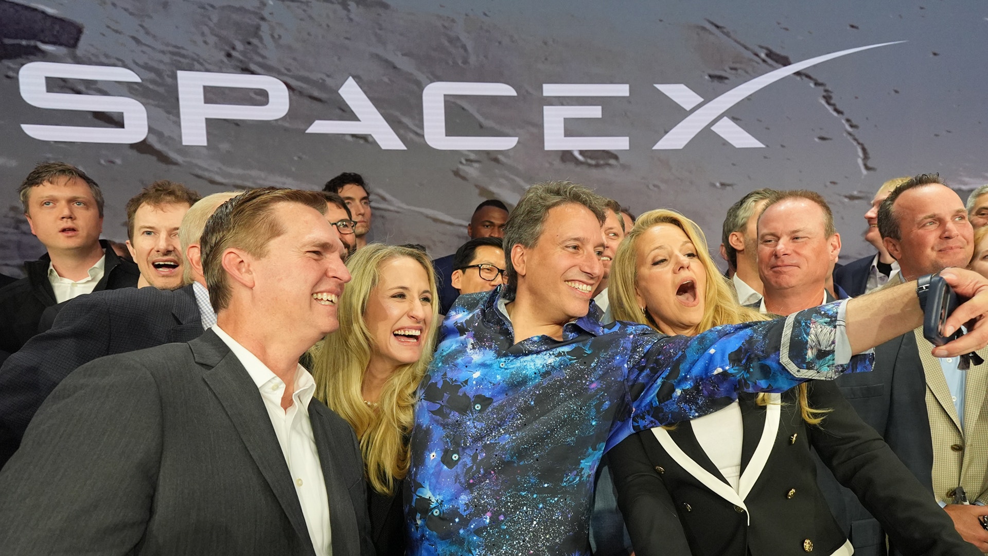 En grupp människor poserar tillsammans framför SpaceX-logotypen. De ser glada och festliga ut.