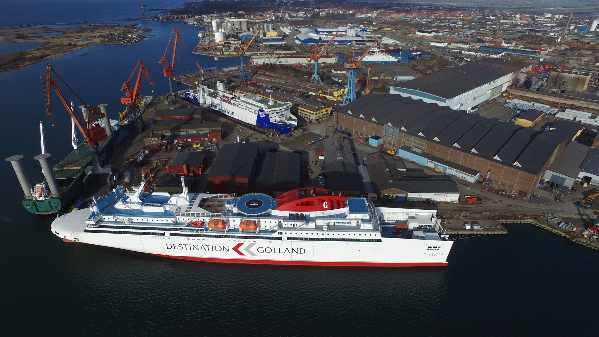 Flygfoto över Öresundsvarvet som visar ett stort varvsområde vid vattnet med dockat passagerarfartyg, industribyggnader, kranar och flera andra fartyg.