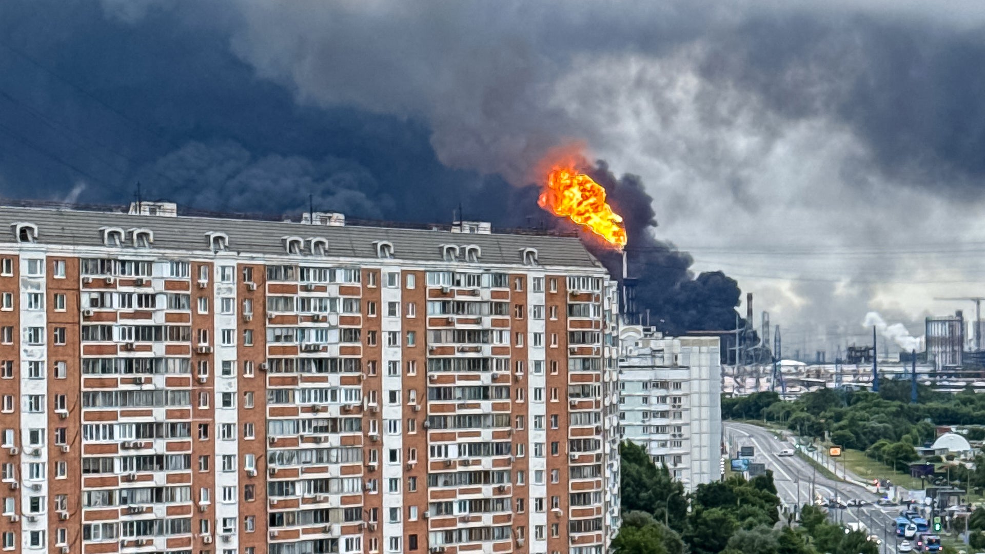 En stor explosion med eldslåga och rök över en industriell anläggning, fotograferad från ett bostadsområde med flervåningshus i förgrunden.