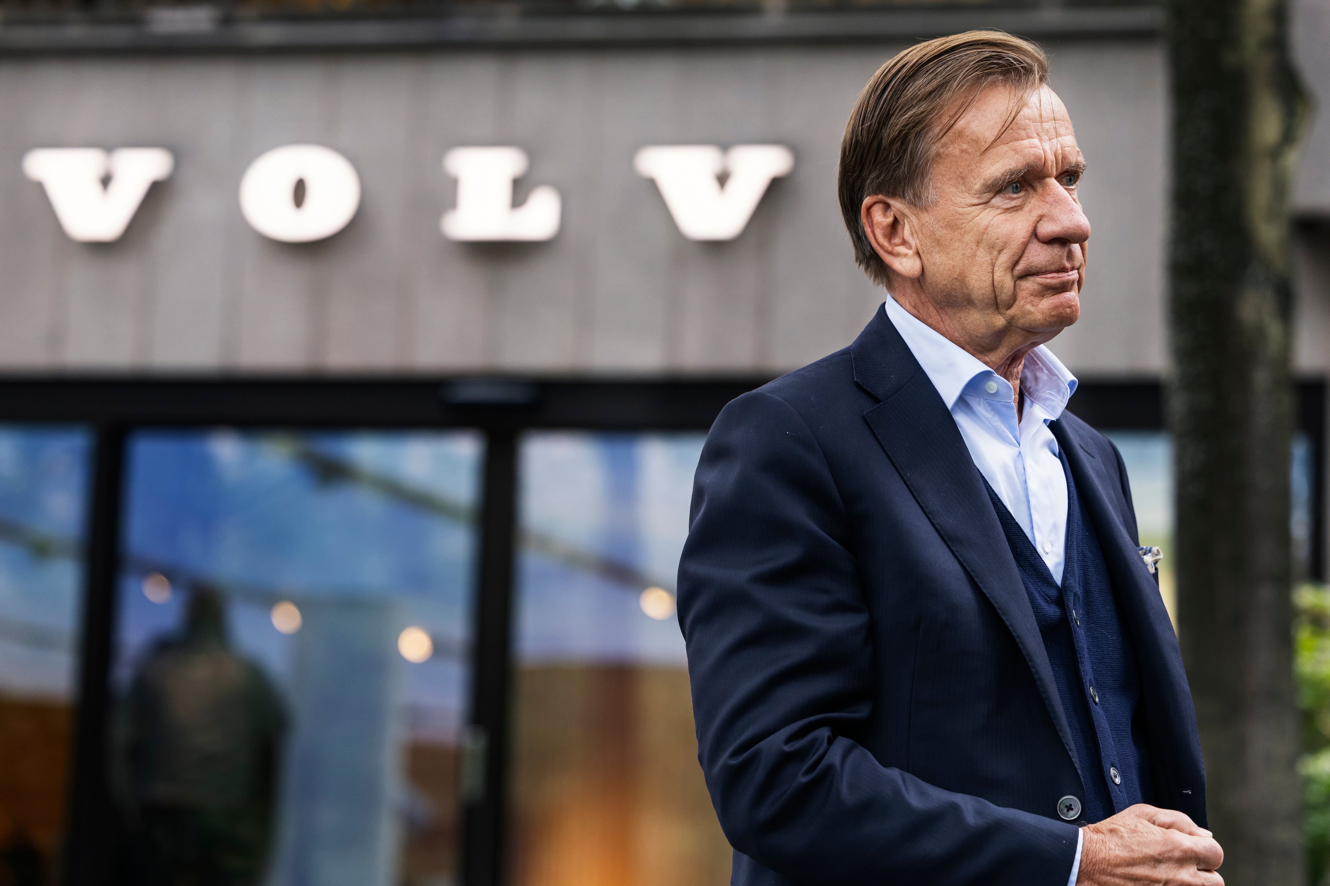 En man i kostym står utomhus framför en byggnad med Volvos logotyp.