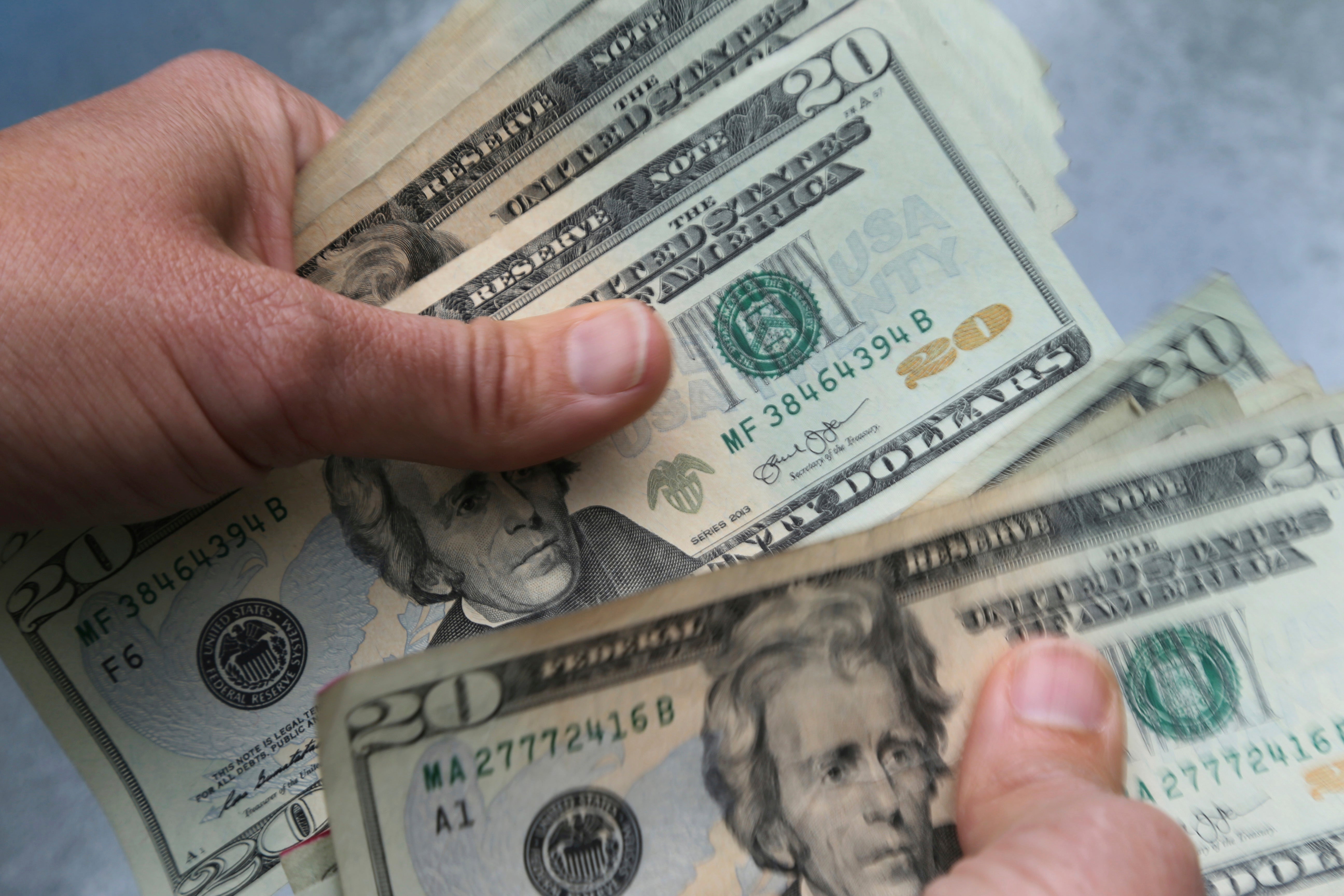 Två händer håller flera amerikanska dollarsedlar.