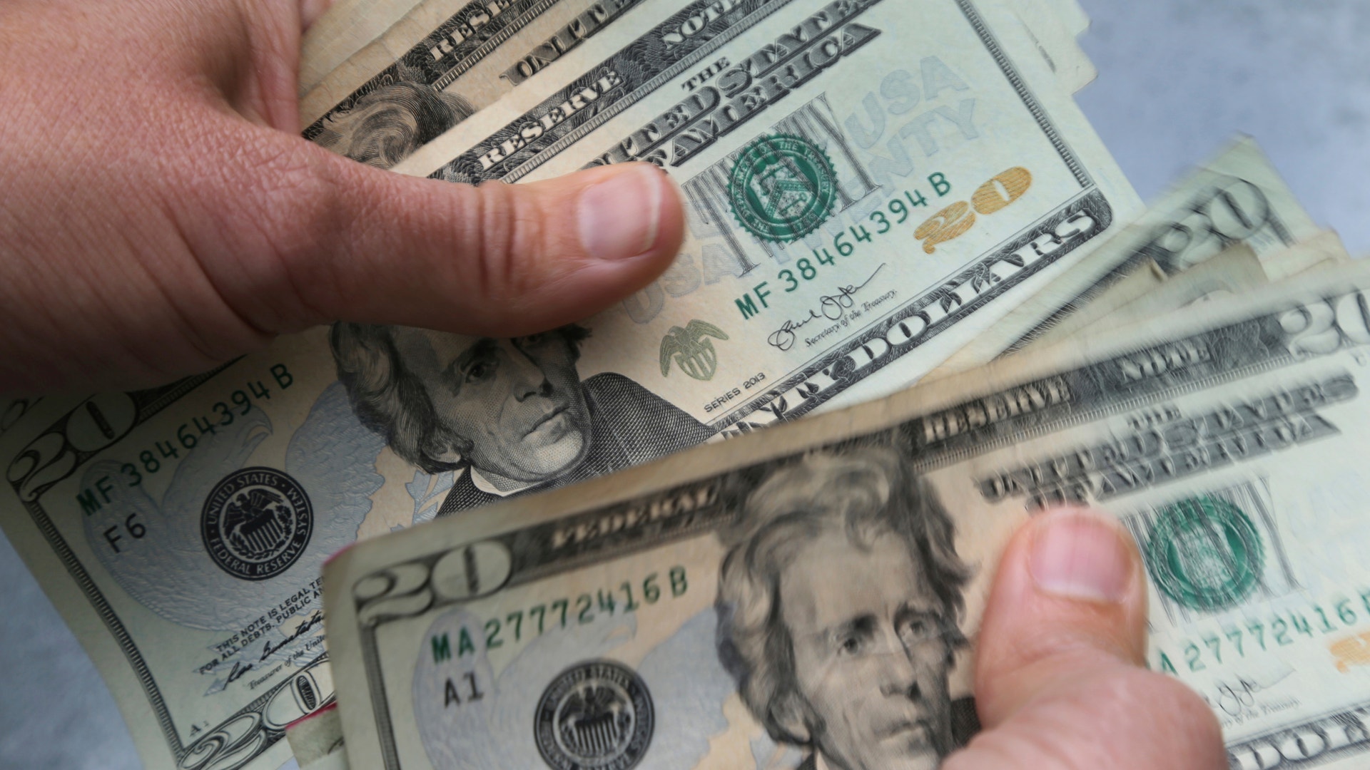 Två händer håller flera amerikanska dollarsedlar.