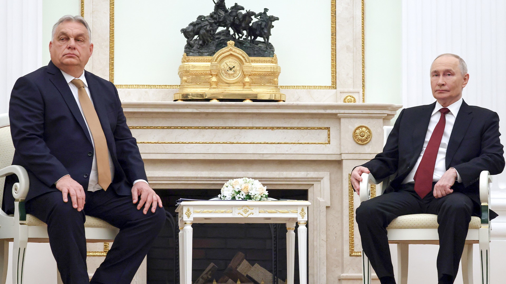 Två män i formell kostym sitter på motsatta sidor av en vit spis i ett klassiskt inrett rum.