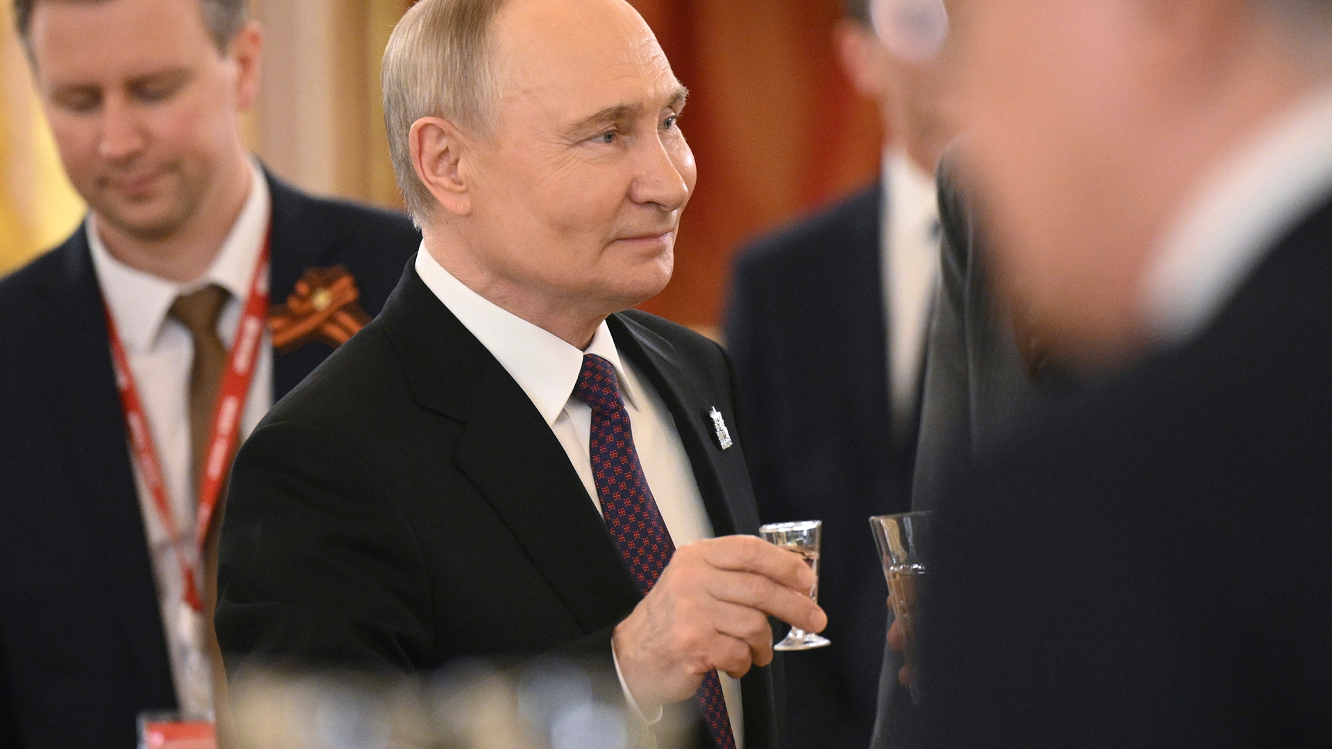 Man i formell kostym och slips på officiell ceremoni omgiven av andra män i kostym.