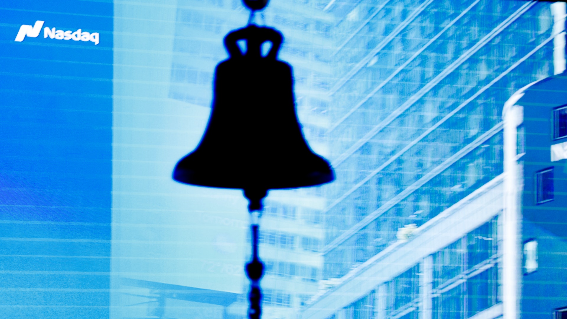 En silhuett av börsklockan framför Nasdaqs logotyp och skyskrapor i blått ljus.