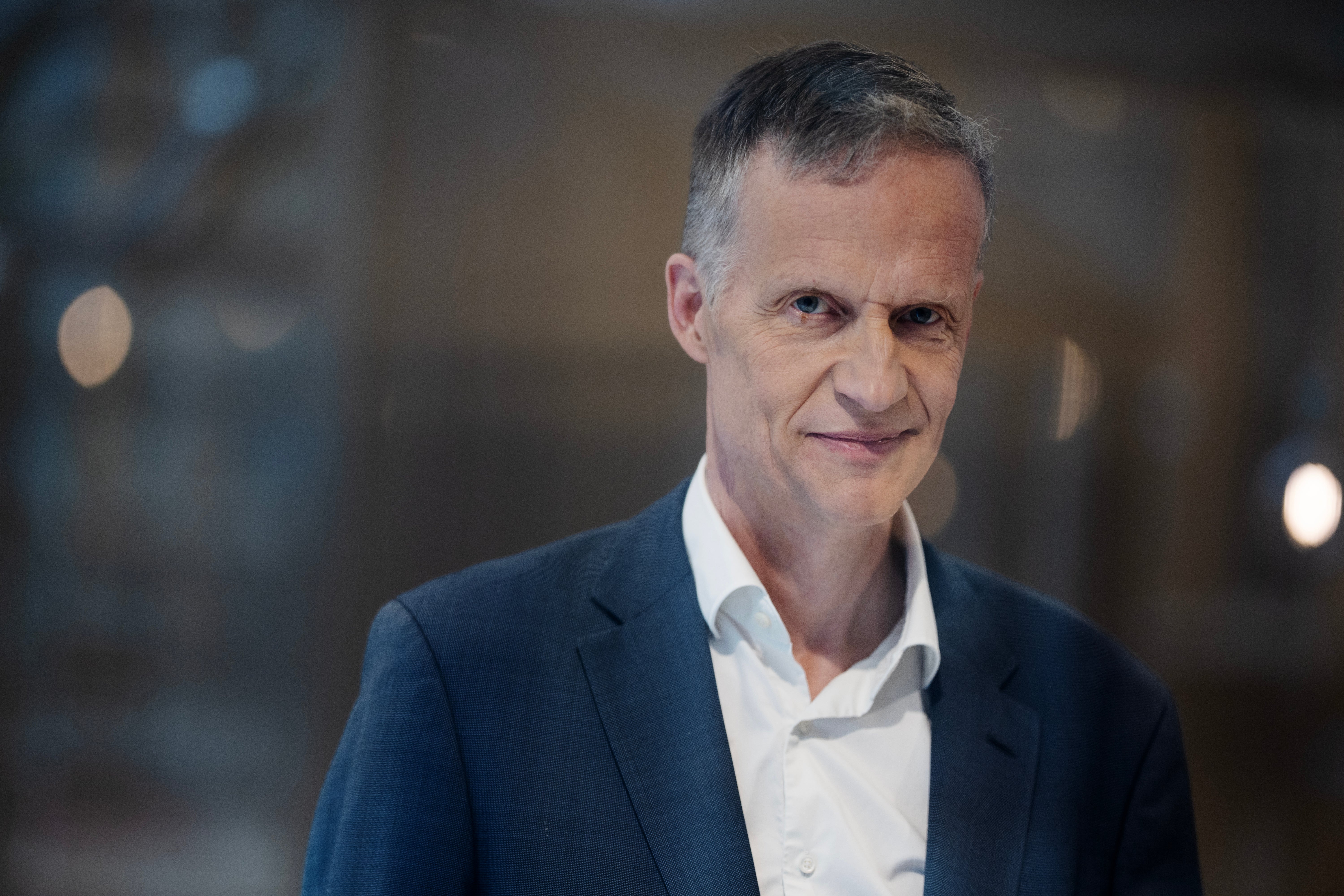 Porträtt av en man i mörkblå kavaj och vit skjorta mot en suddig bakgrund.
