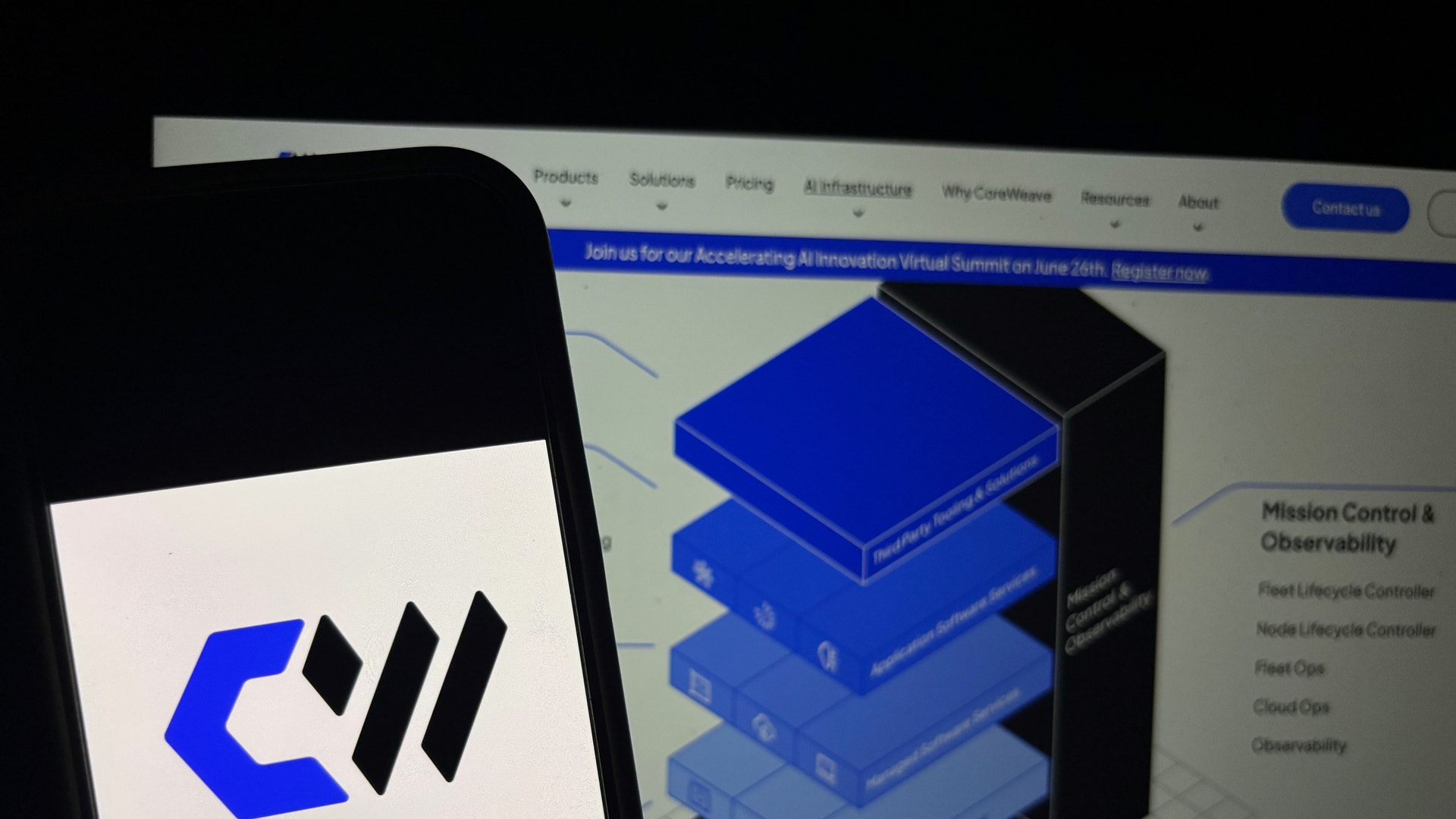 Mobiltelefon med Coreweaves logotyp framför en datorskärm som visar företagets webbplats.