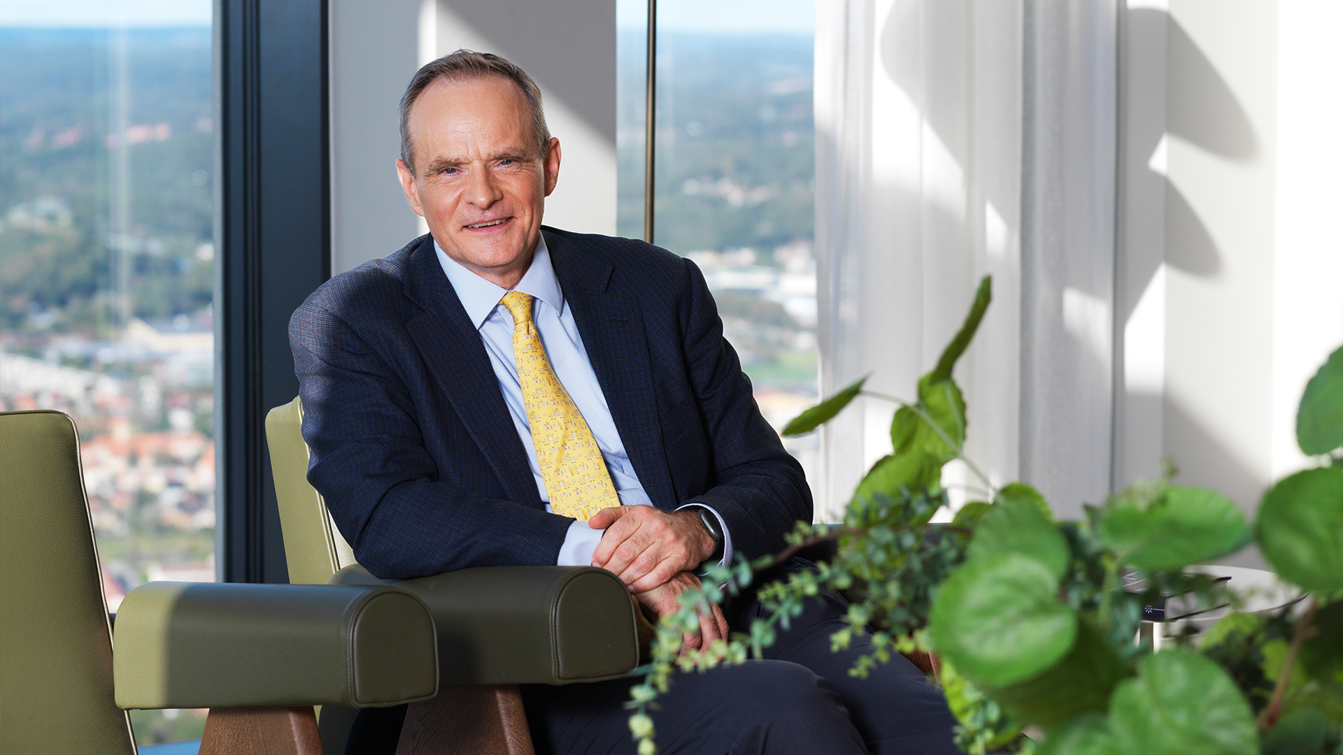 Simon Johnson sitter i kostym på en läderfåtölj. Han är i en ljus lägenhet i Göteborg.