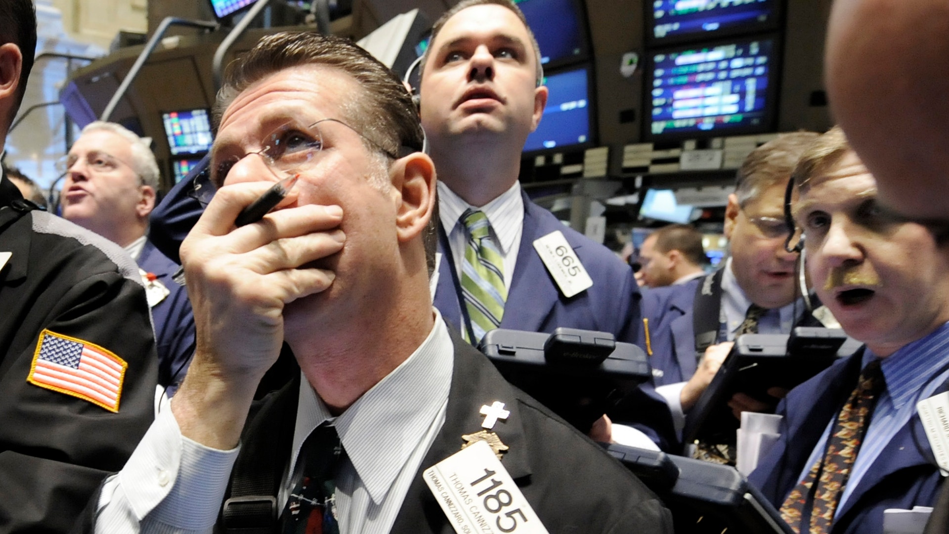 Handlare på en aktiebörs med bekymrad uppsyn, omgivna av kolleger och handelsskärmar i bakgrunden.