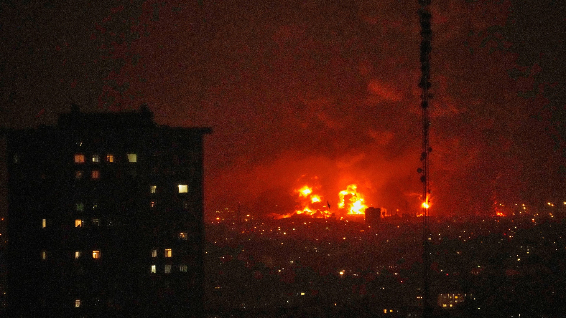 Nattlig stadsbild med brander och explosioner på horisonten