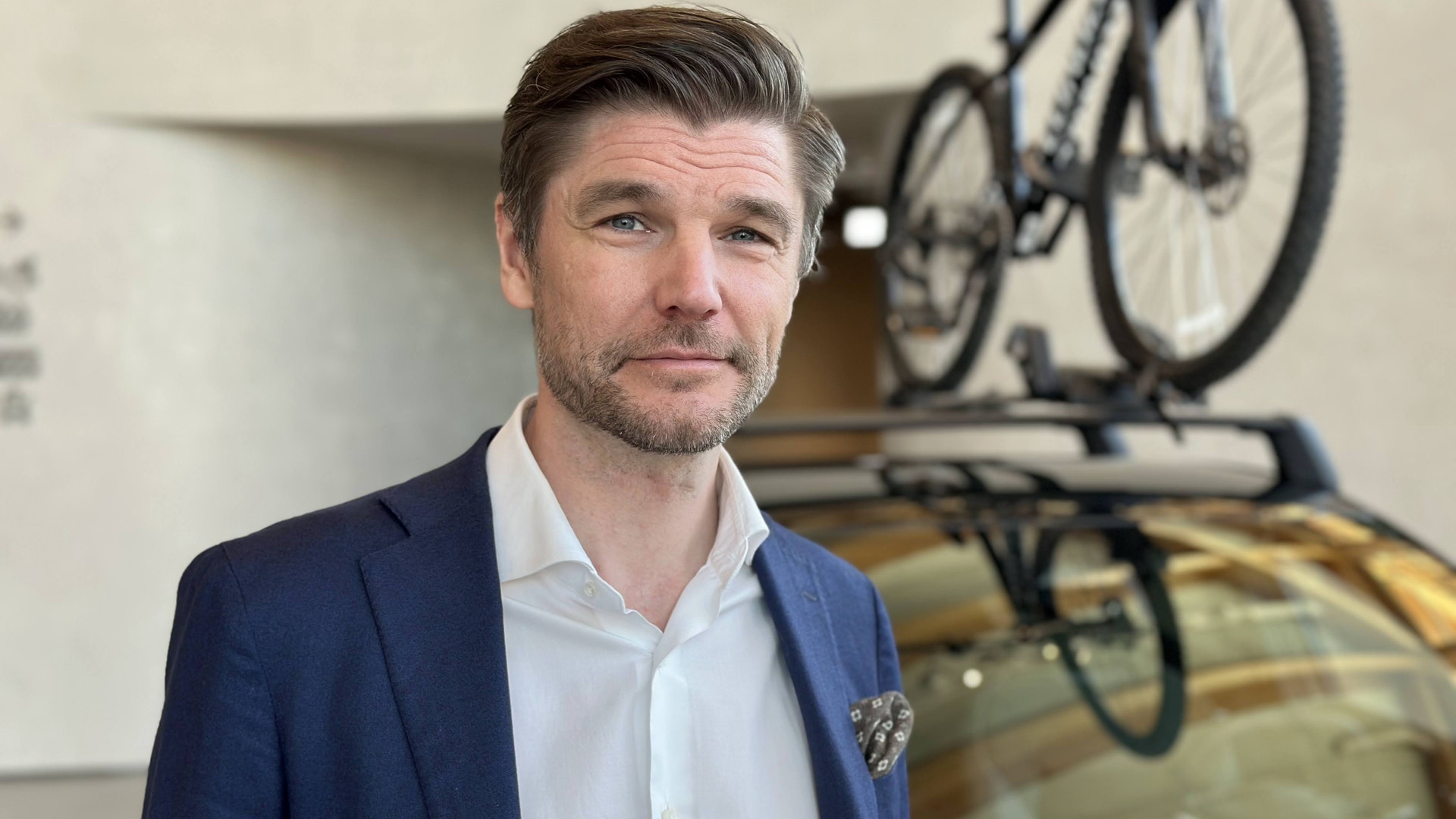Porträtt av en man i blå kavaj och vit skjorta. I bakgrunden syns en cykel monterad på en vägg.