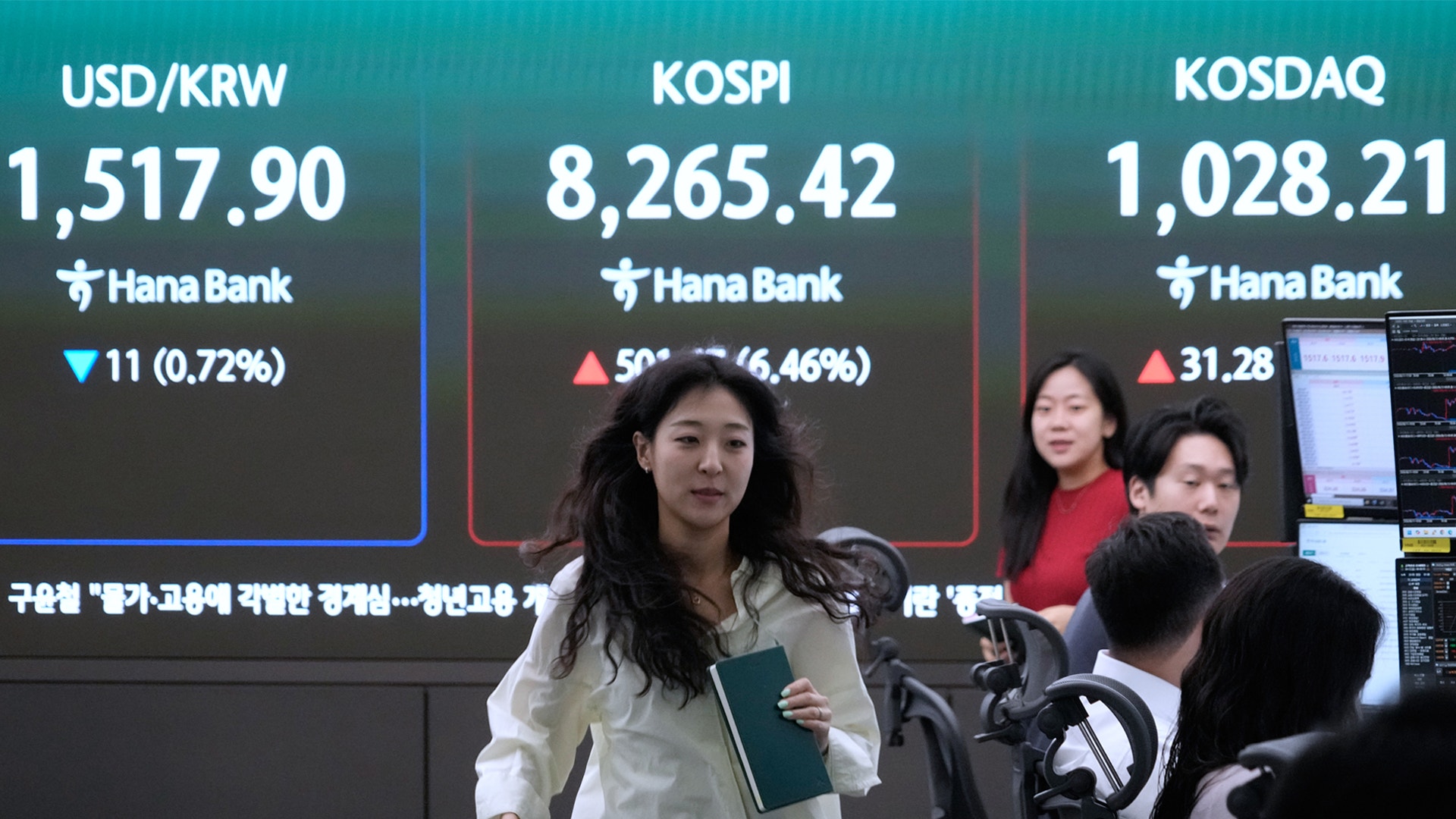 Kvinna i vit skjorta framför skärm som visar börsdata och valutakurser från Hana Bank