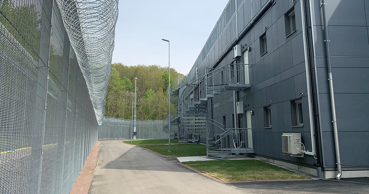 Extern vy av en modern kriminalvårdsanstalt med säkerhetsstängsel och grå institutionsbyggnader längs en väg. Anstalten är placerad i Högsbo, i Göteborg.