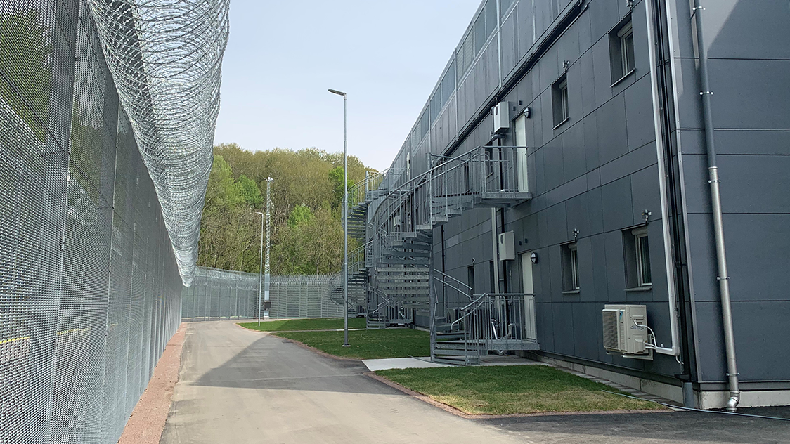 Extern vy av en modern kriminalvårdsanstalt med säkerhetsstängsel och grå institutionsbyggnader längs en väg. Anstalten är placerad i Högsbo, i Göteborg.