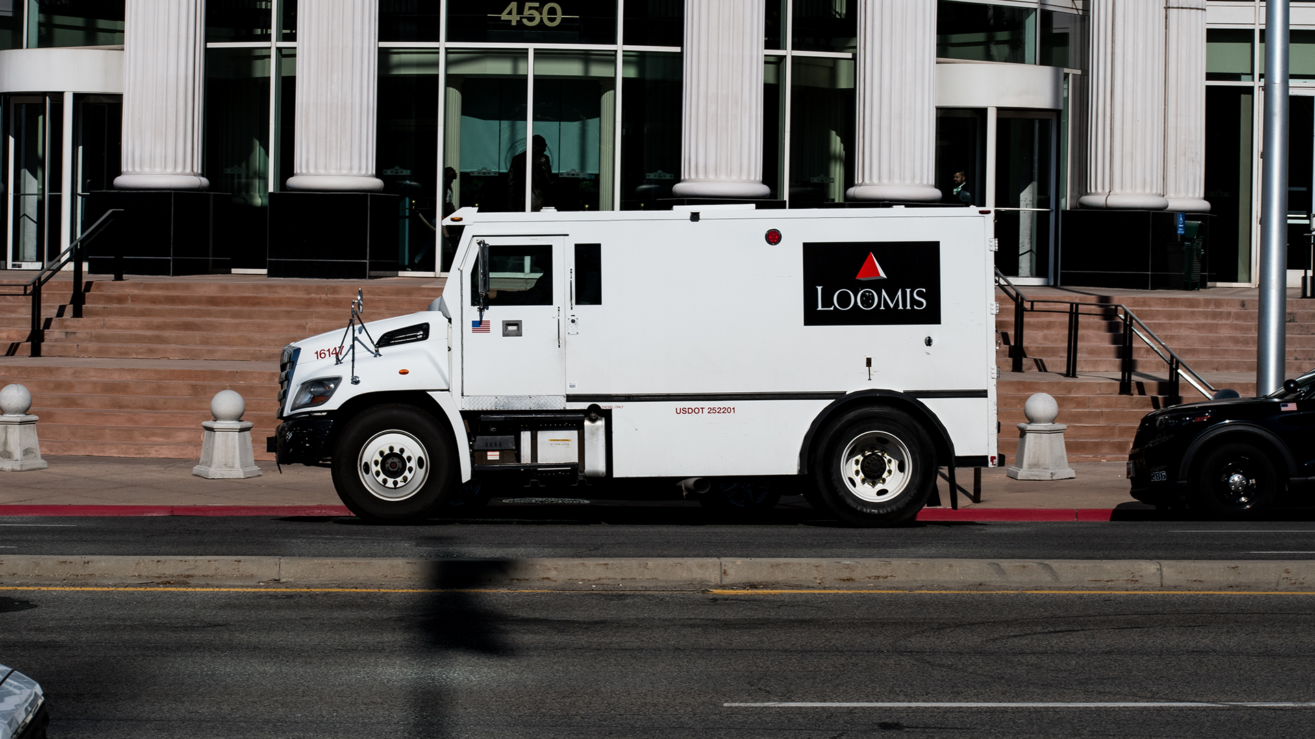 Vit Loomis-värdebil parkerad på gata framför byggnad med vita kolonner