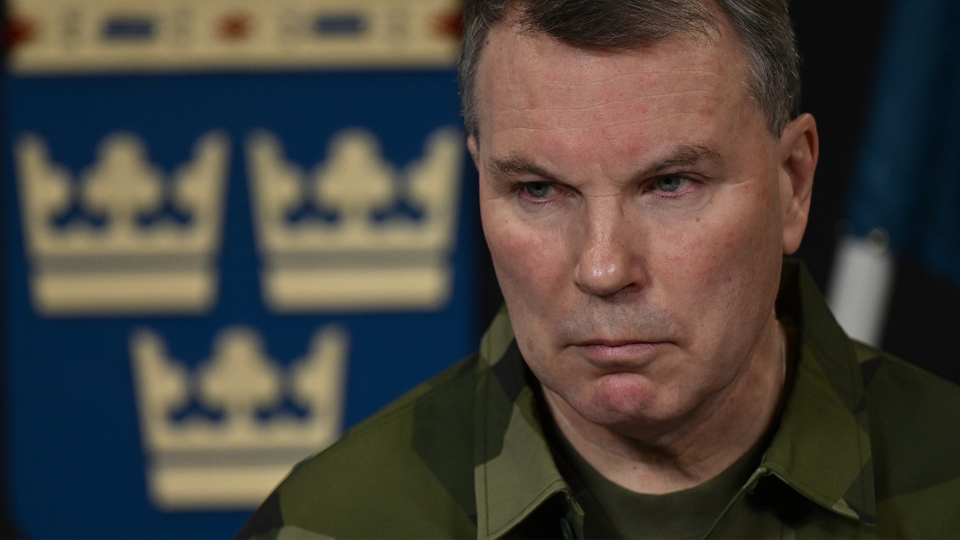 Thomas Nilsson i militär uniform framför en blå bakgrund med svenska kronor.