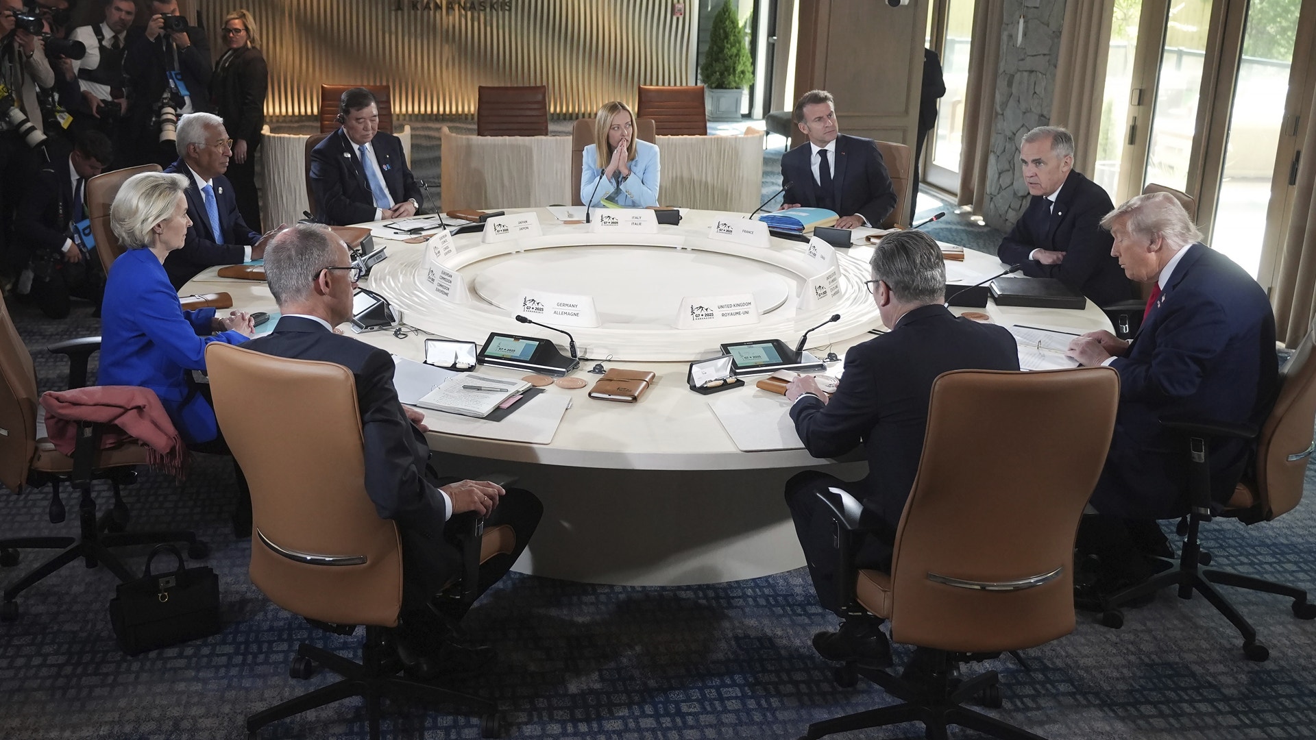 Grupp av affärspersoner samlade runt ett stort runt bord under ett möte i en modern konferenssal.