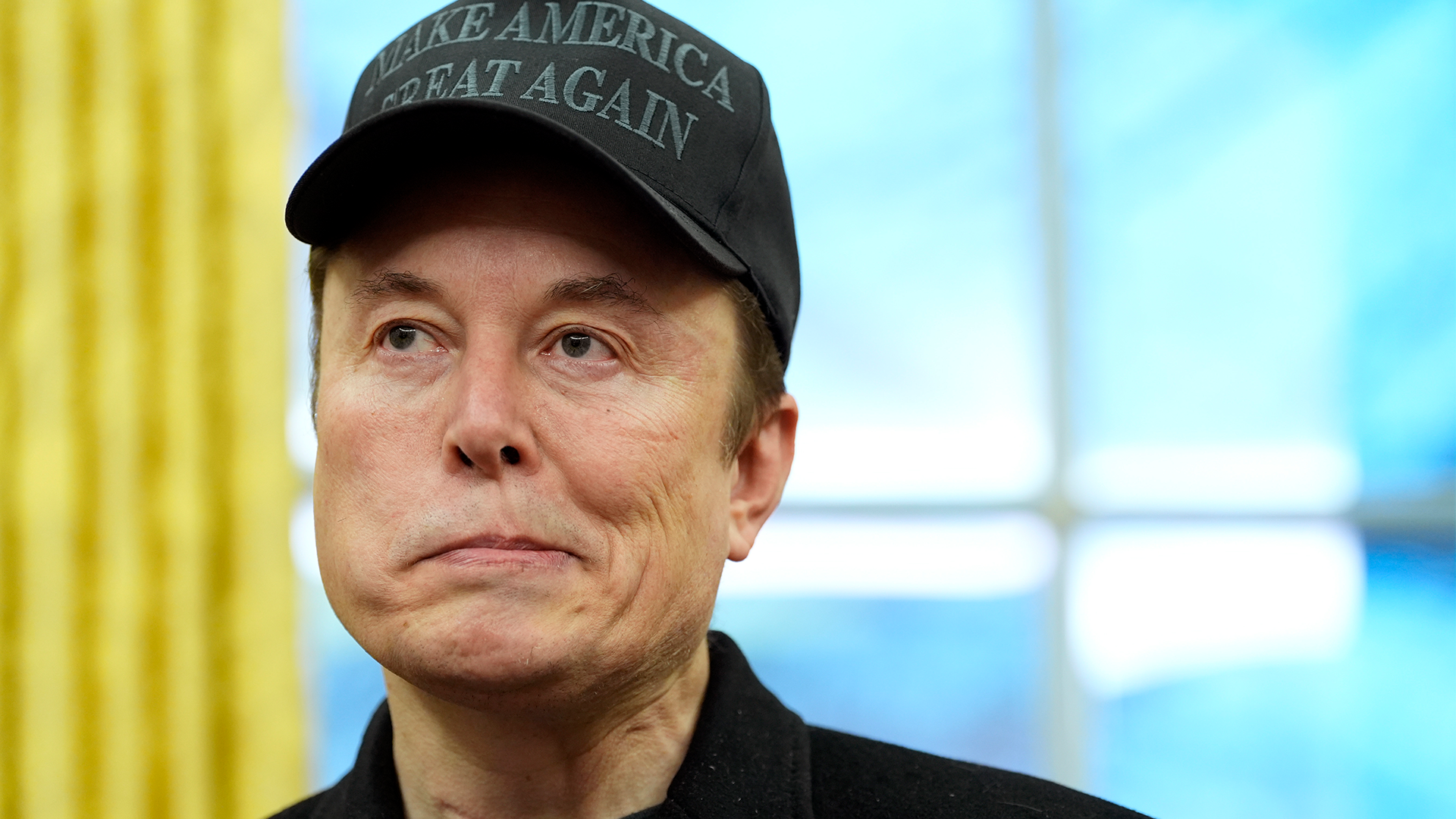 Elon Musk ser förtvivlad ut i en svart "Make america great again"-keps.