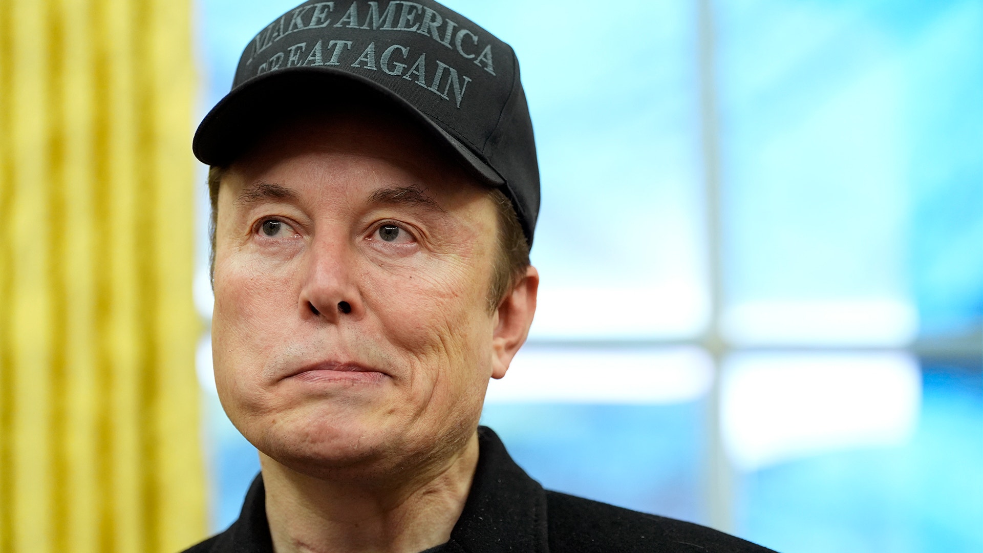 Elon Musk ser förtvivlad ut i en svart "Make america great again"-keps.
