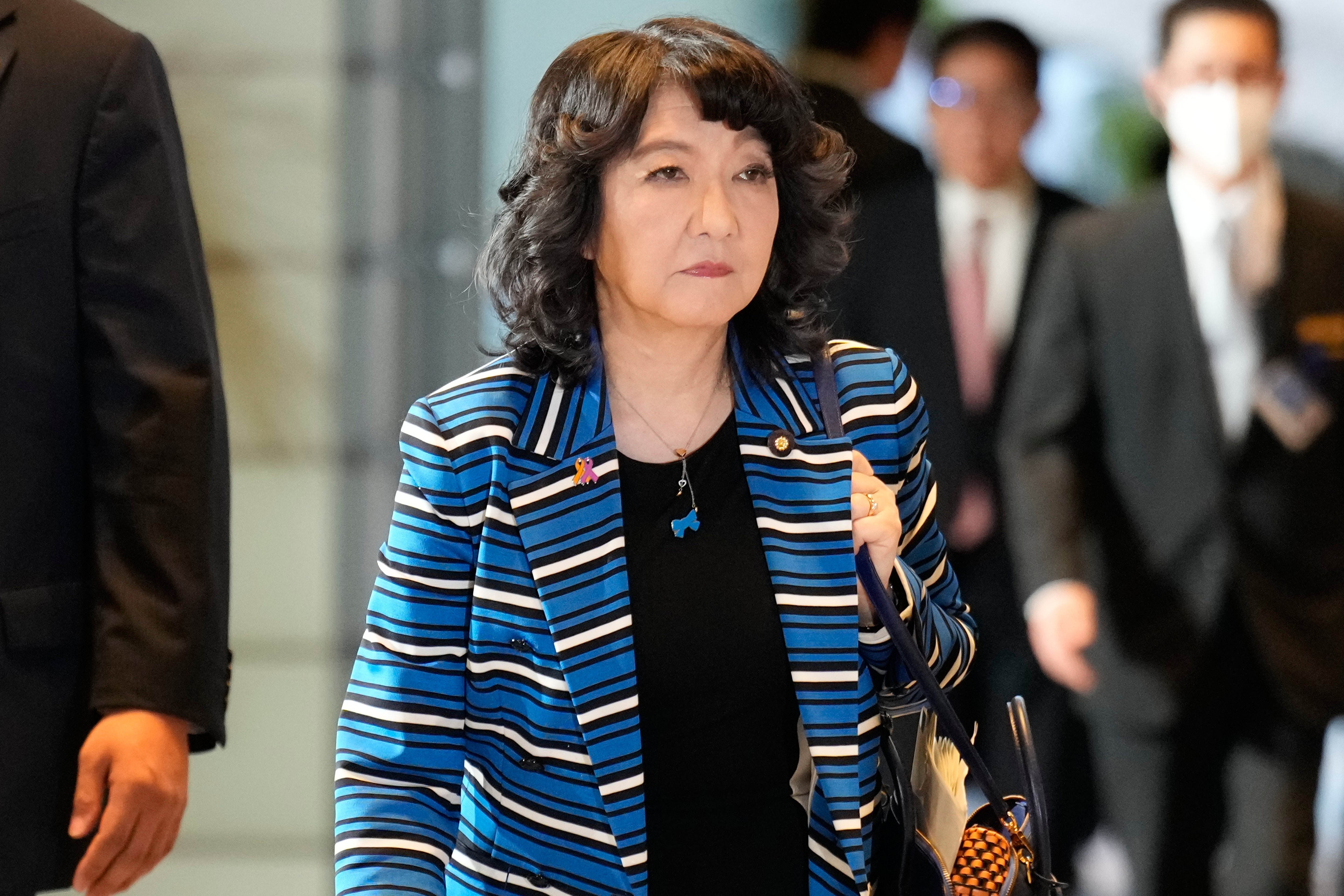 En kvinna i blå och vit randig blazer går genom en korridor med andra människor i bakgrunden.