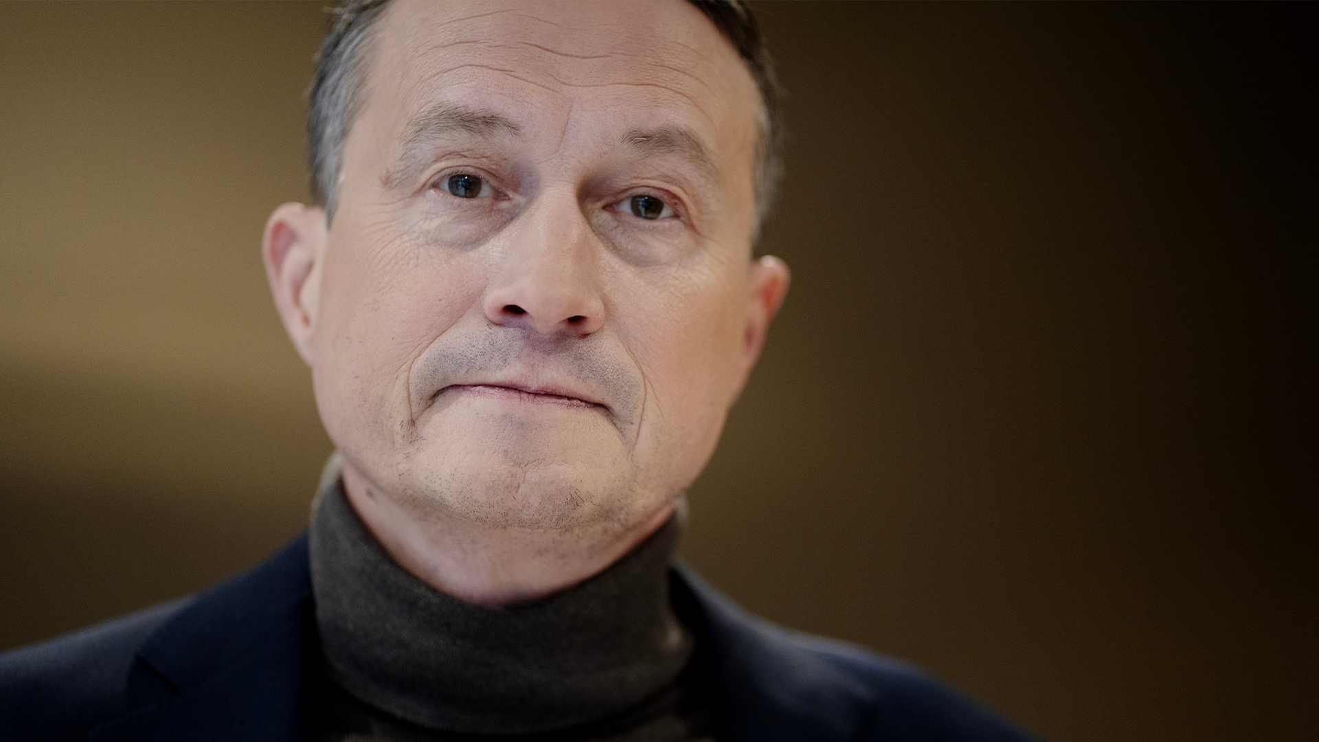 Porträttfoto av en man med mörkblå tröja mot en suddig bakgrund