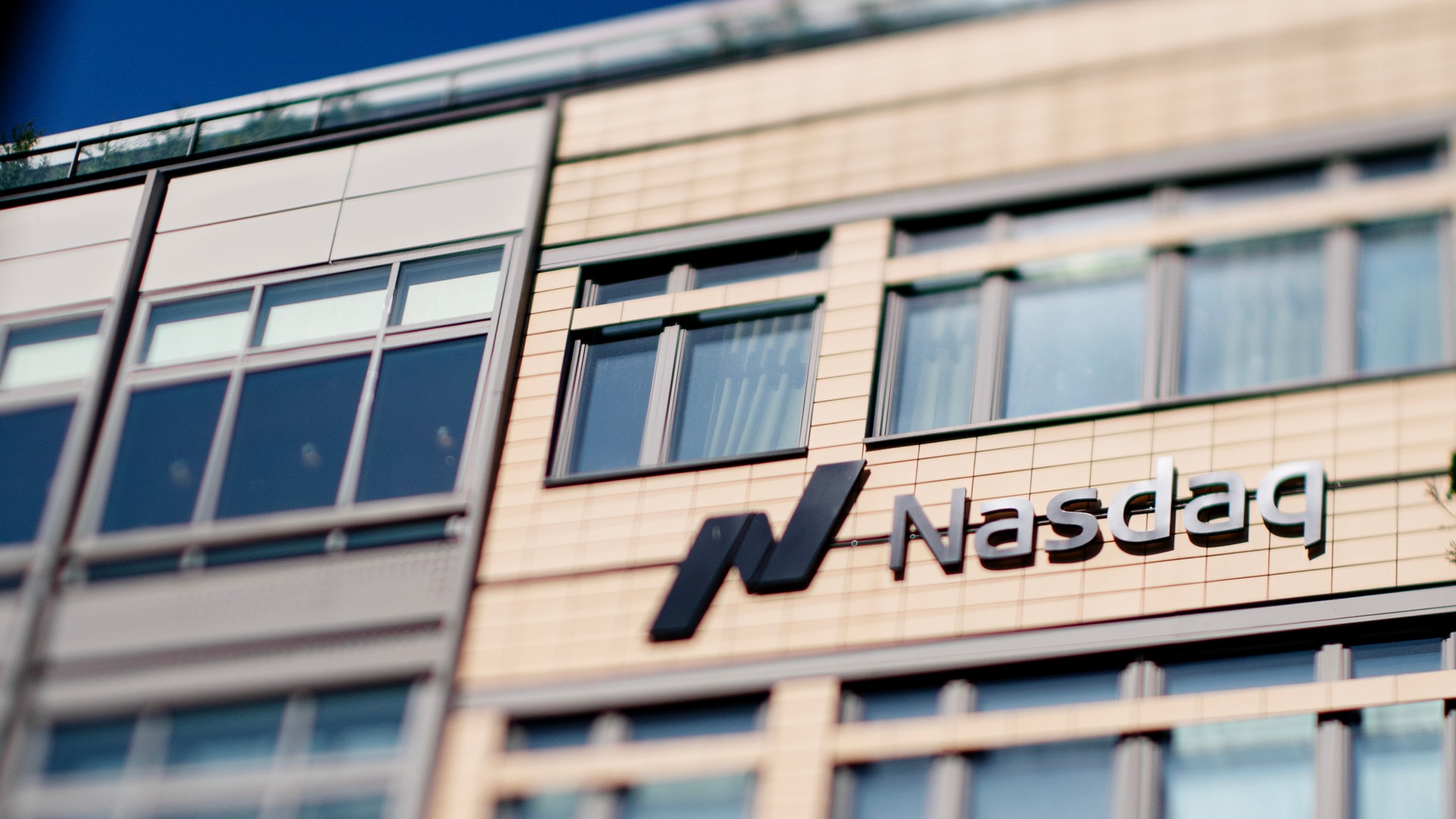 Nasdaq-logon på fasaden av en modern kontorsbyggnad med ljusa väggar och många fönster.