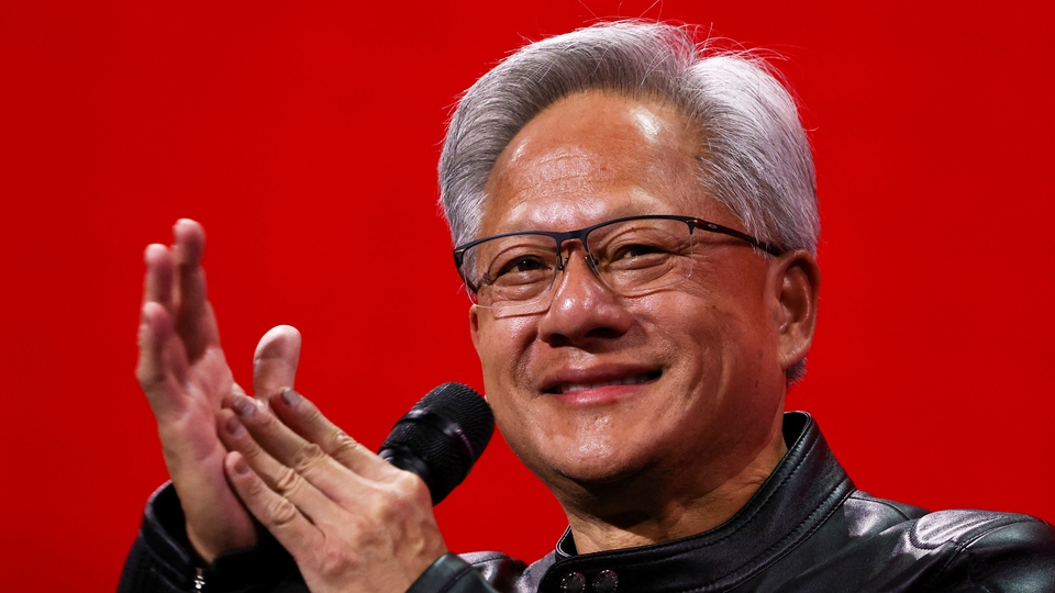 Nvidia:s vd Jensen Huang klappar händerna och ler till publiken när han står på en röd scen med en mikrofon i handen.