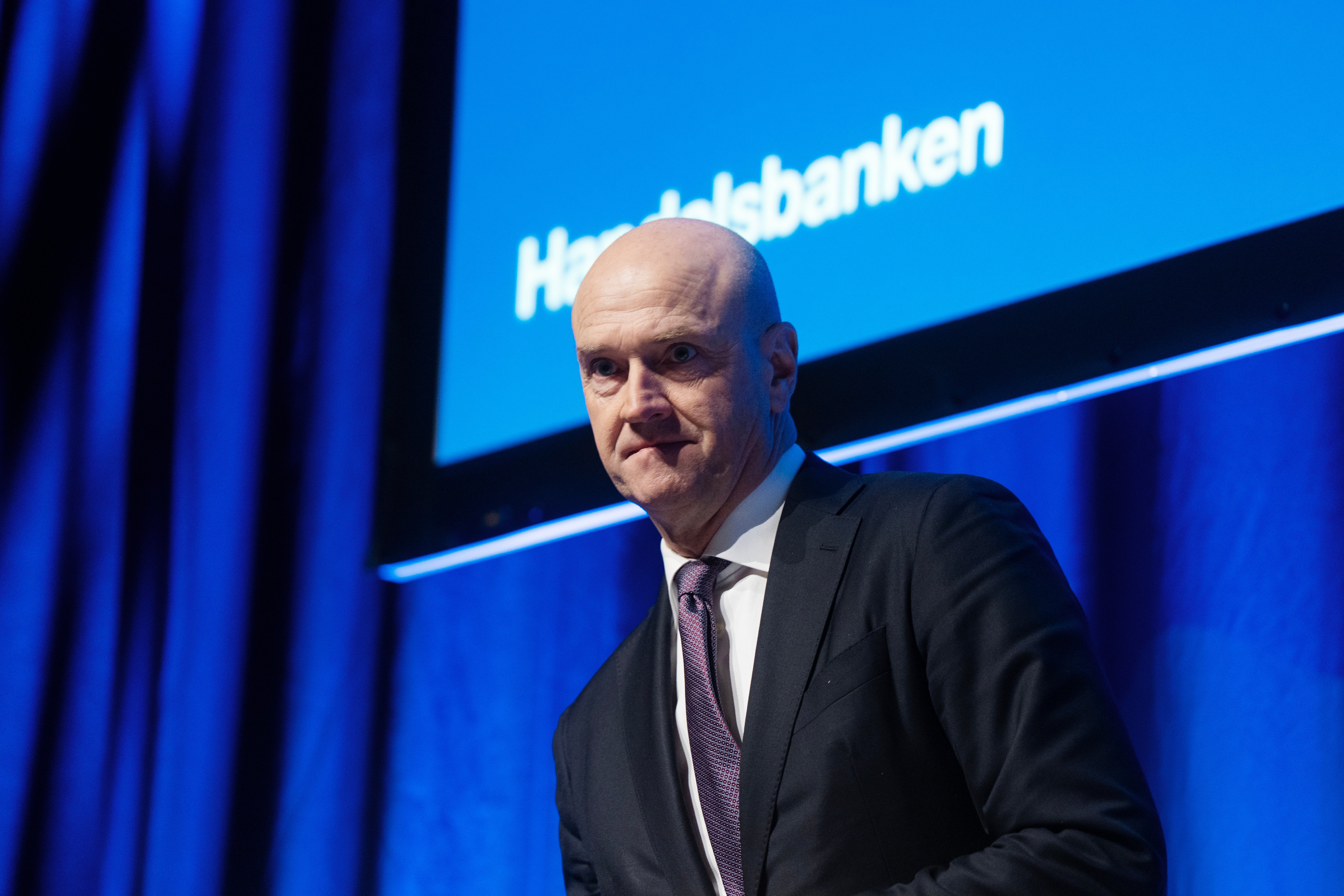 En man i kostym och slips framför en blå bakgrund med Handelsbanken-logotyp