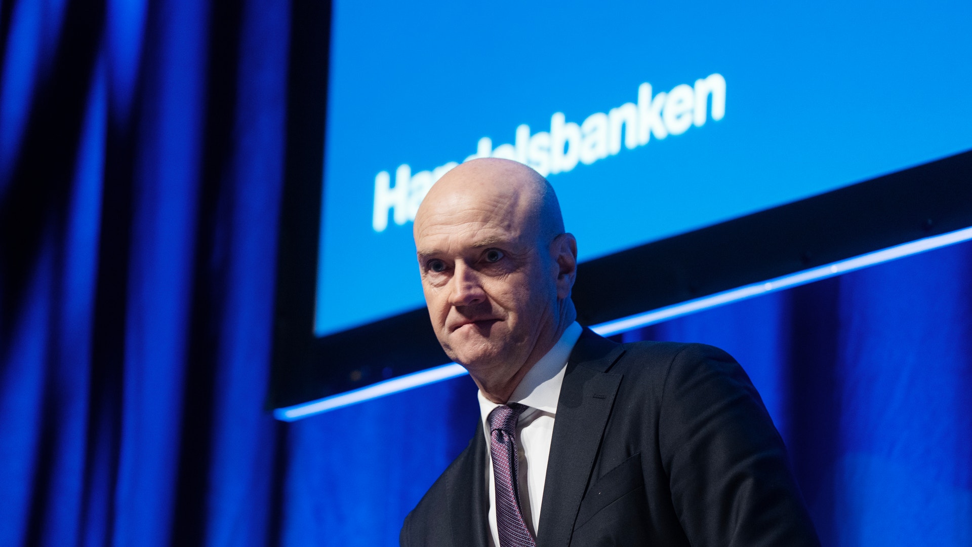 En man i kostym och slips framför en blå bakgrund med Handelsbanken-logotyp