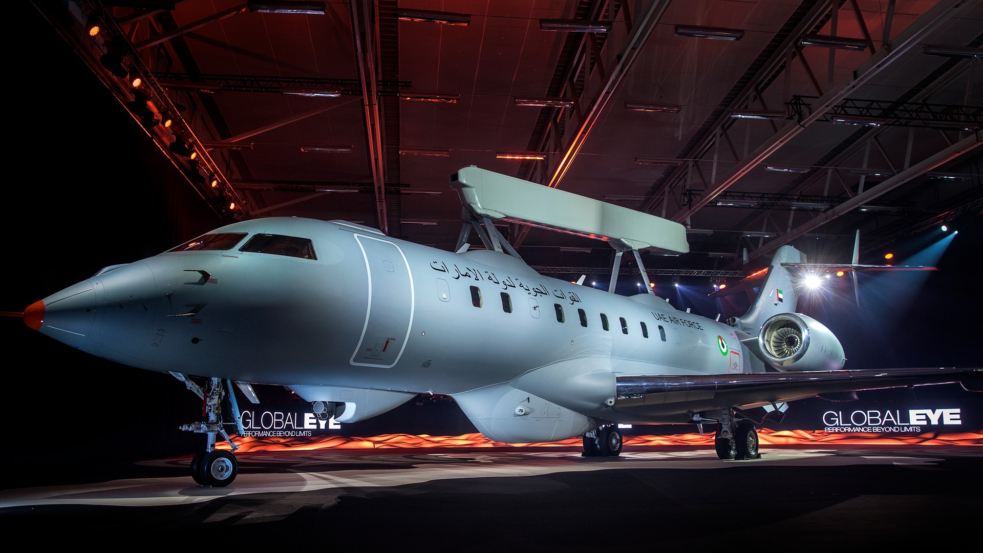 Ett modernt vitt passagerarflygplan står i en hangar under röd och blå belysning.
