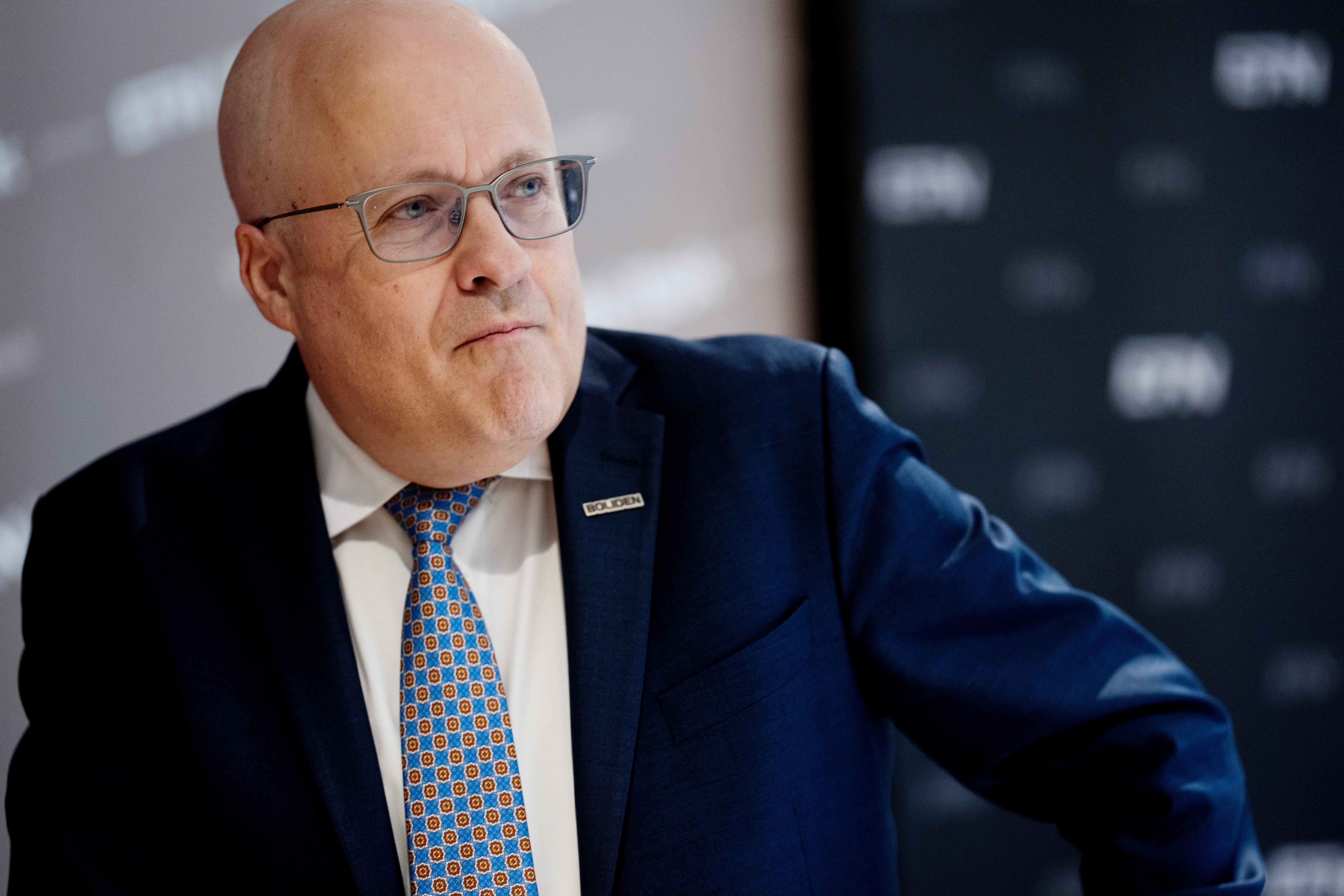 Porträtt av en man i blå kostym och glasögon som ser ut mot sidan.