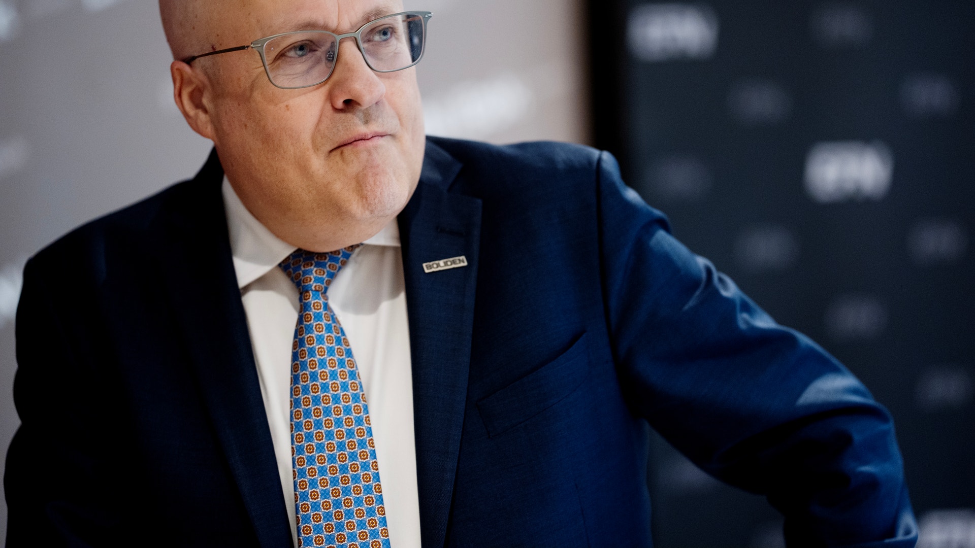 Porträtt av en man i blå kostym och glasögon som ser ut mot sidan.