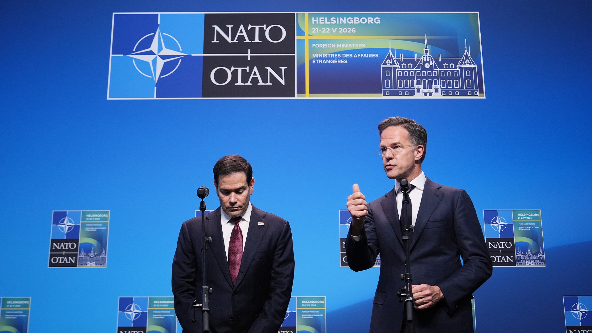 Två män i kostym talar på en scen under en NATO-konferens i Helsingborg 2024. Blå bakgrund med NATO-logon och konferenslogotyper syns bakom dem.