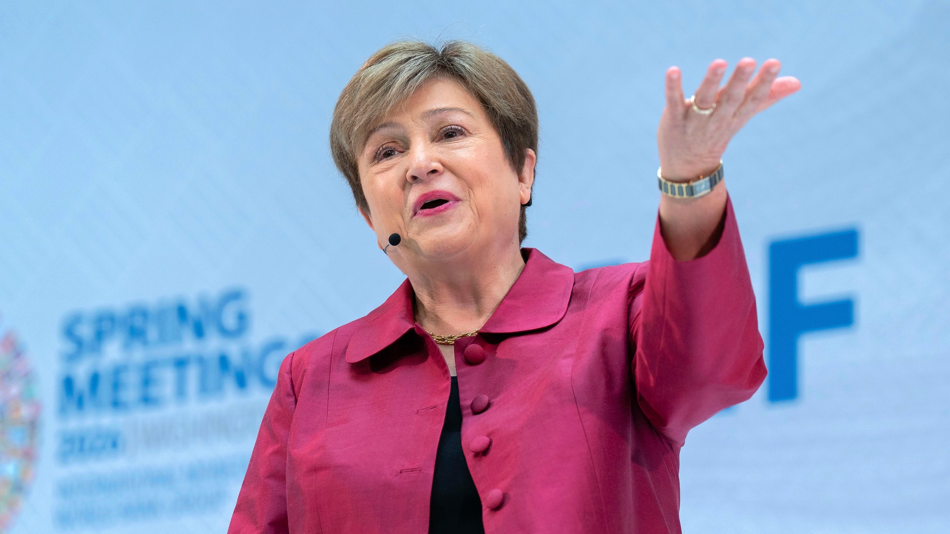 En kvinna i rosa jacka håller ett tal på en konferens och gestikulerar medan hon talar.