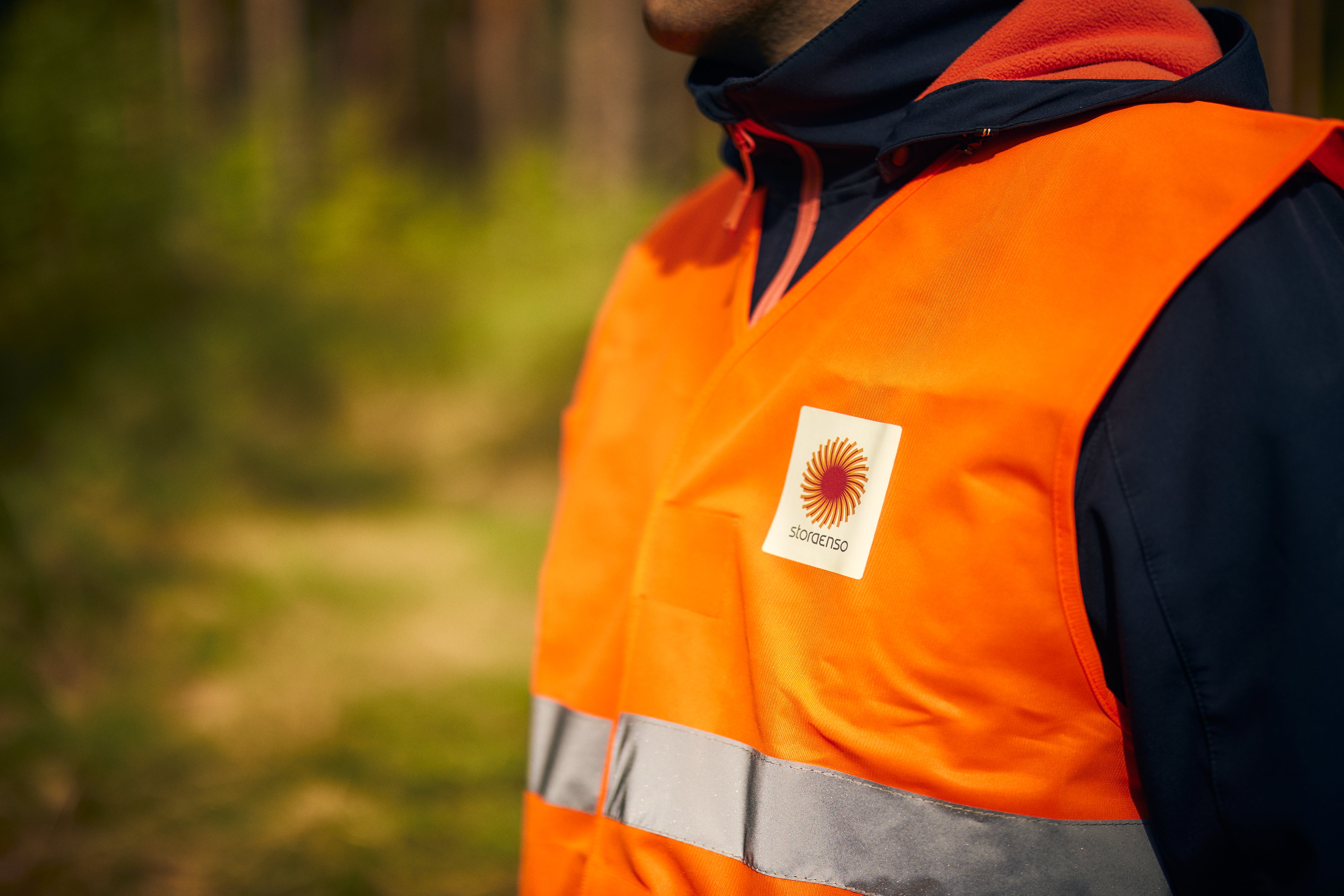 Person i orange arbetsvest med Stora Enso-logotyp och reflekterande band.