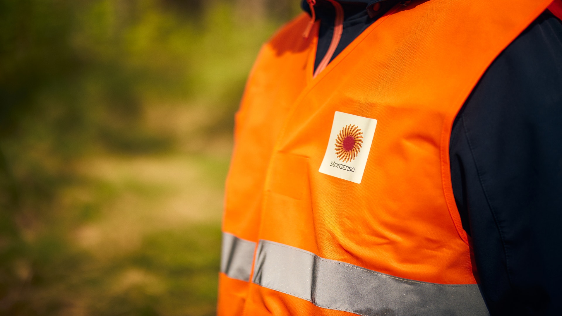 Person i orange arbetsvest med Stora Enso-logotyp och reflekterande band.