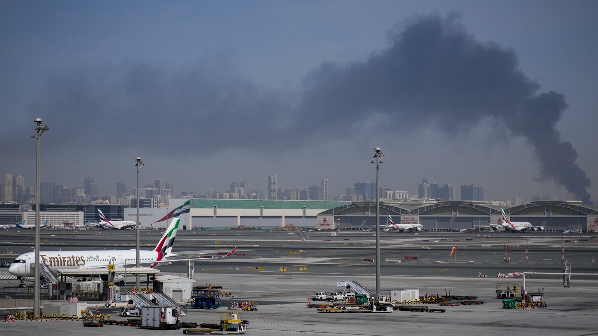 Flygplats med Emirates-plan parkerat vid terminalen, stadsskyline i bakgrunden