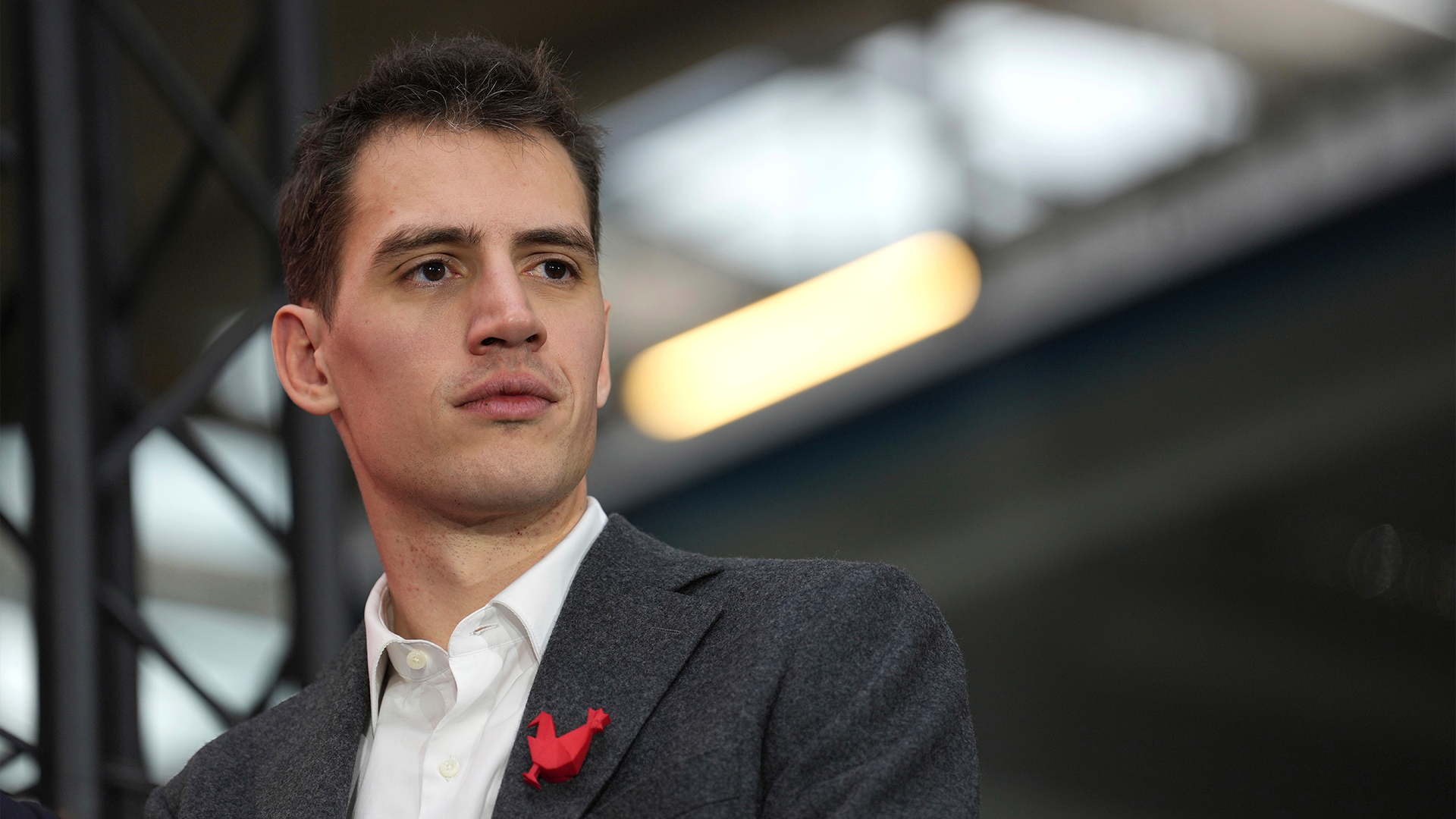 Porträtt av en man i mörkgrå kostym och vit skjorta med en röd blomma på kavajkragen.