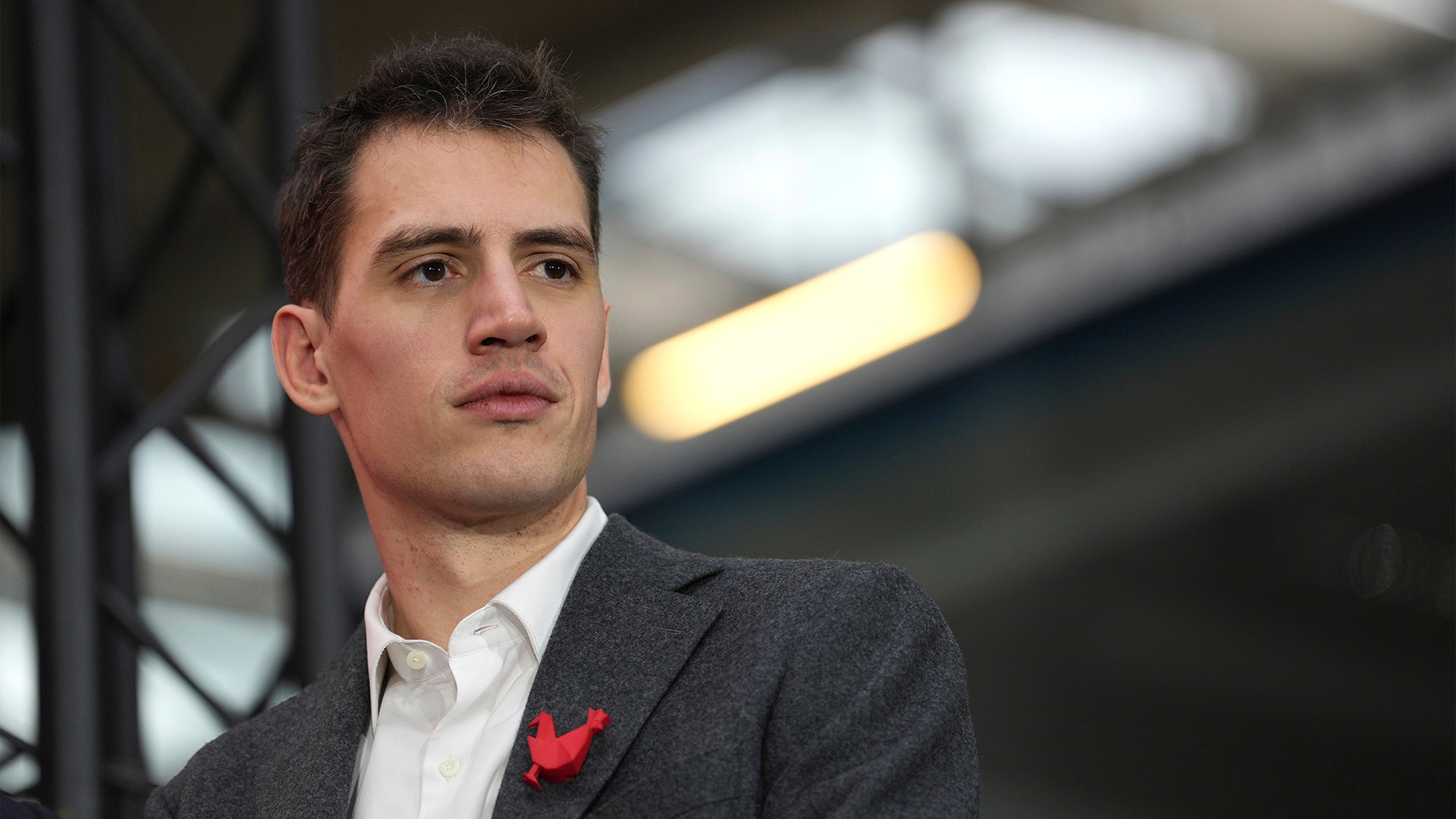 Porträtt av en man i mörkgrå kostym och vit skjorta med en röd blomma på kavajkragen.