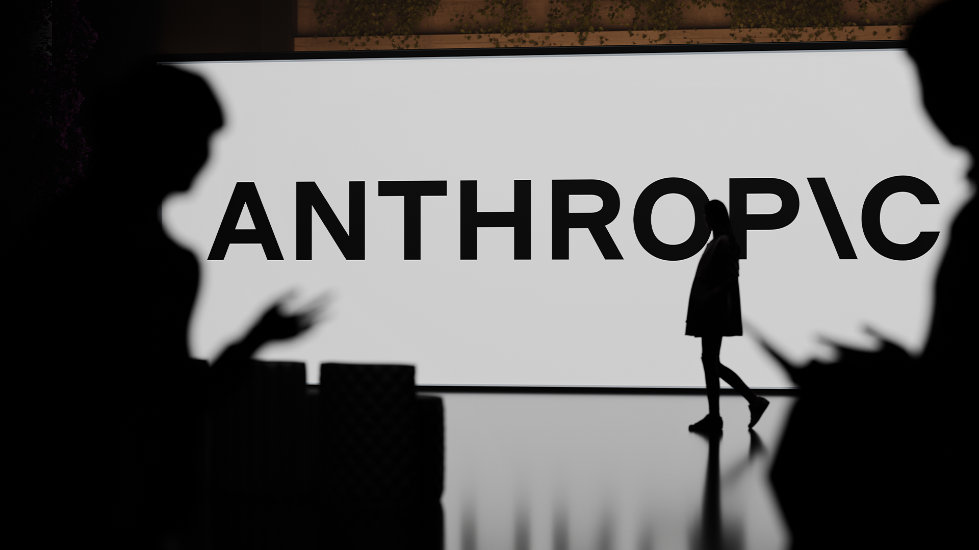 Silhuetter av människor i ett modernt interiör med texten "ANTHROPIC" på en vägg