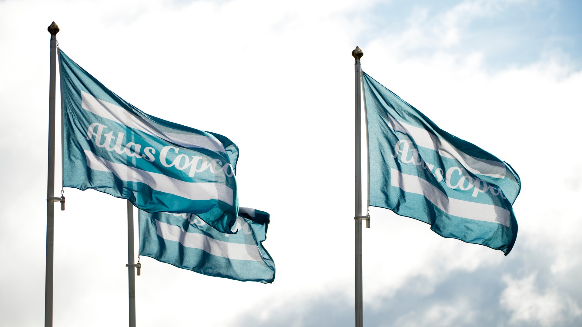 Två teal- och vitrandiga flaggor som vajar mot en molnig himmel