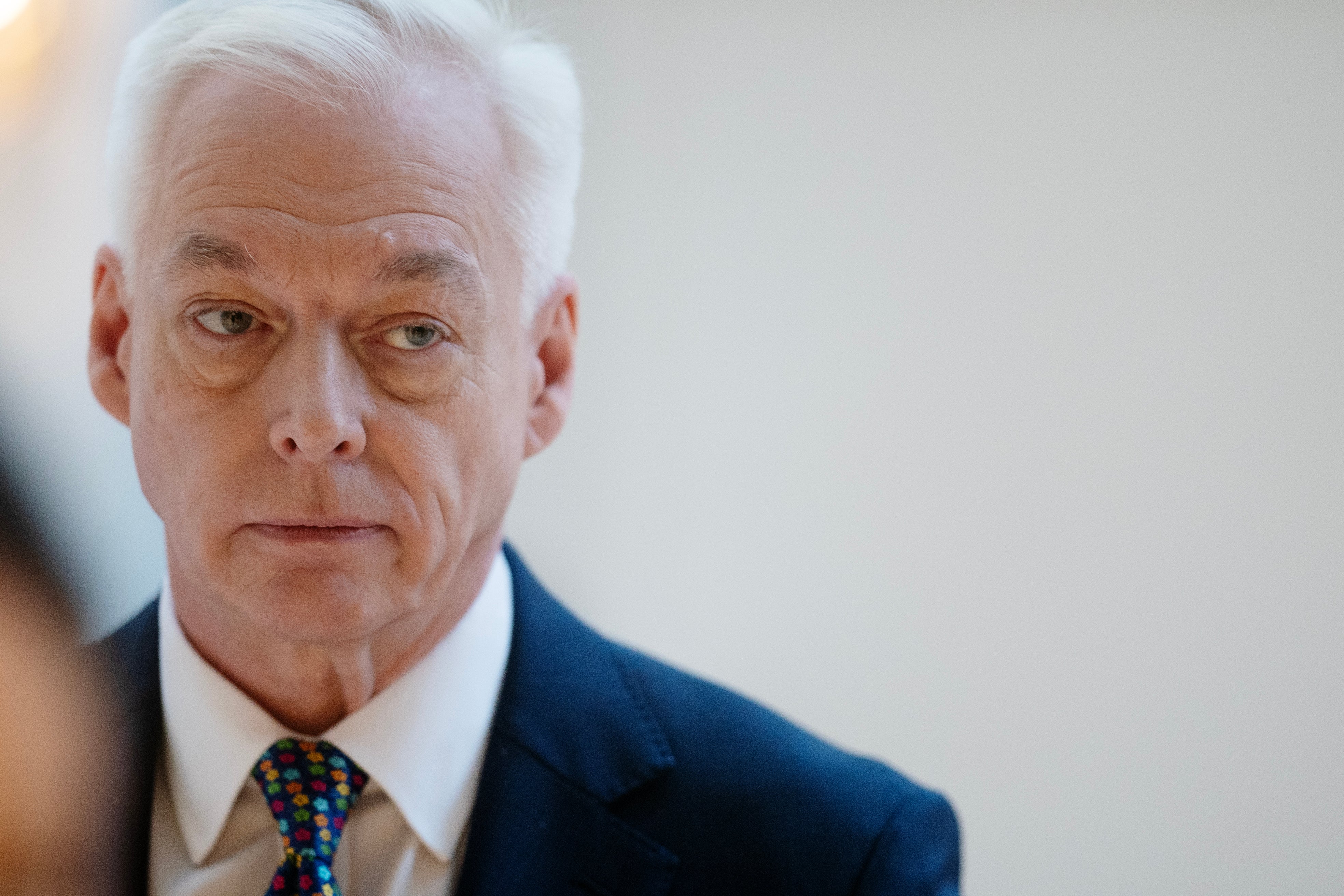 Porträttfoto av en äldre man med vitt hår, iklädd mörkblå kostym och färgglad slips.