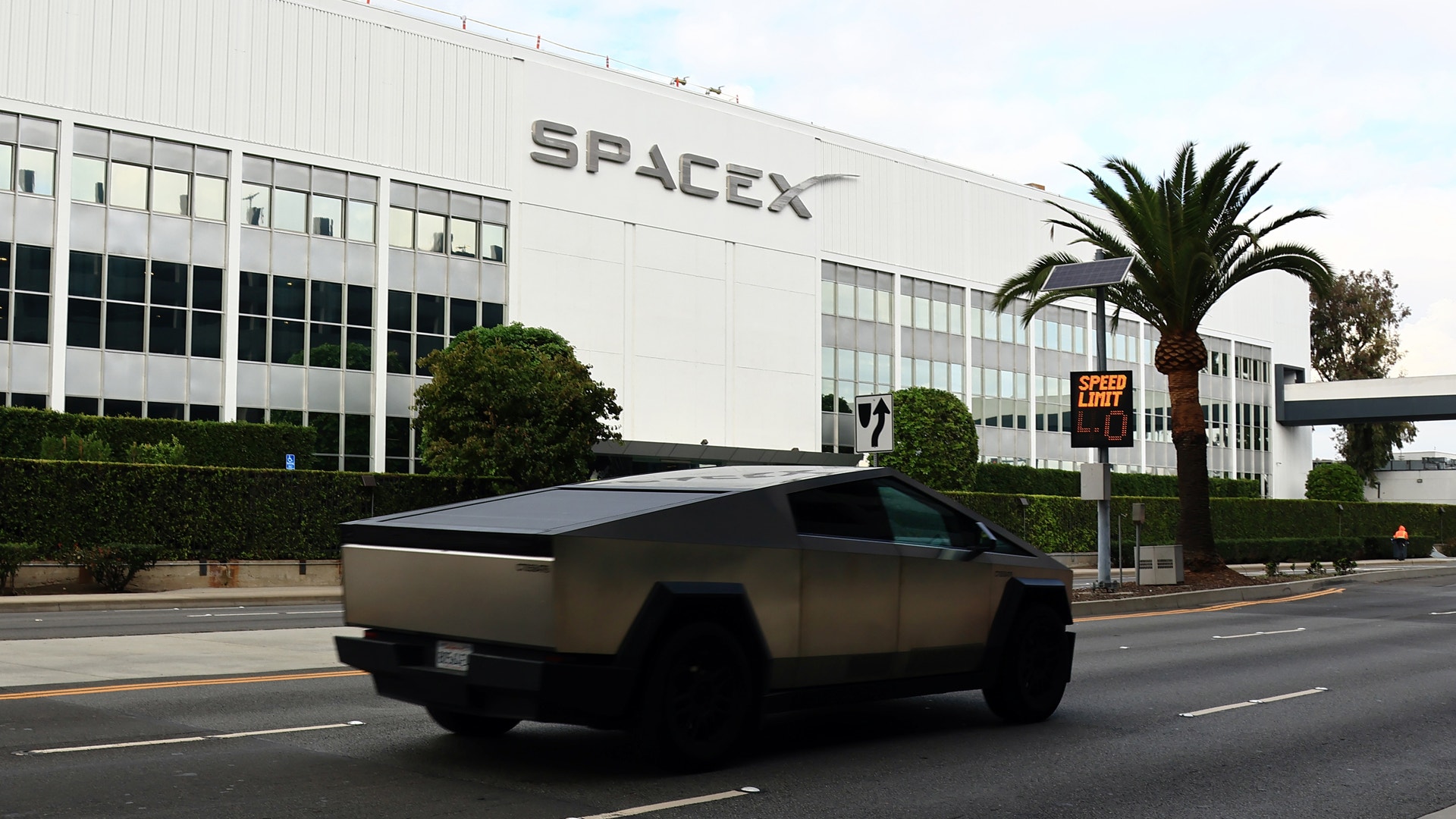 En futuristisk bil kör förbi en stor industribyggnad med SpaceX-logotypen.