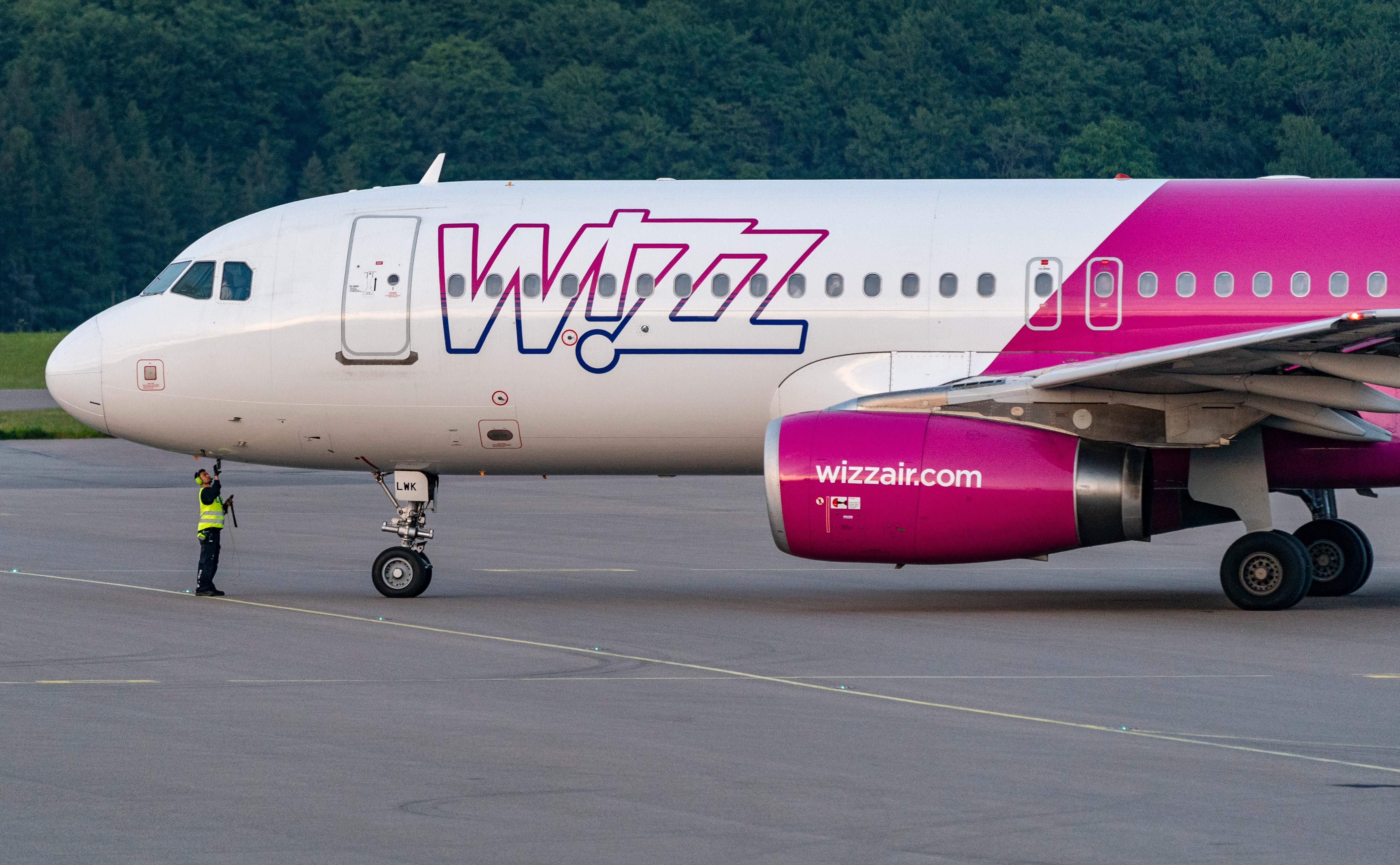 Wizz Air-flygplan parkerat på landningsbanans betongyta med en markarbetare i gul väst i närheten.