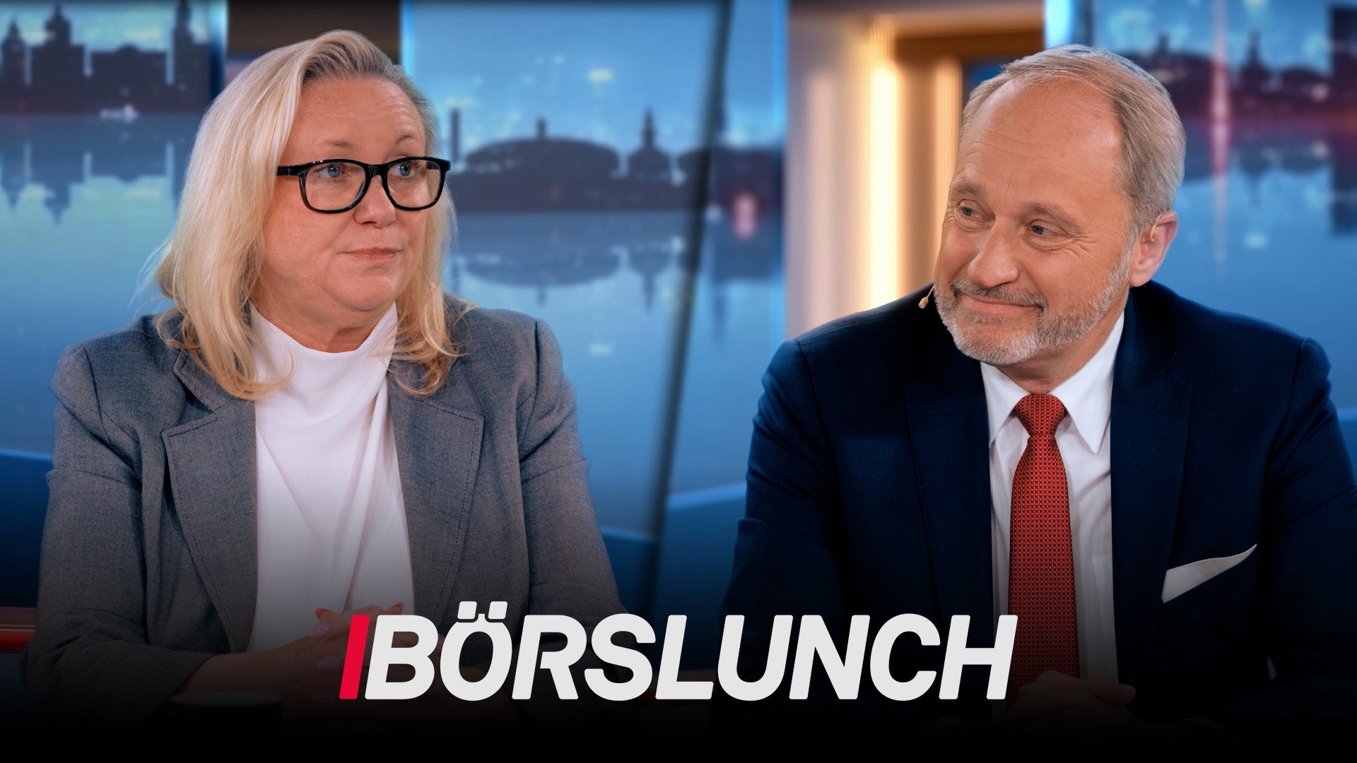 Två personer sitter vid ett skrivbord i en TV-studio. Bakom dem syns en stadshorisont. Texten Börslunch visas längst ned på skärmen.