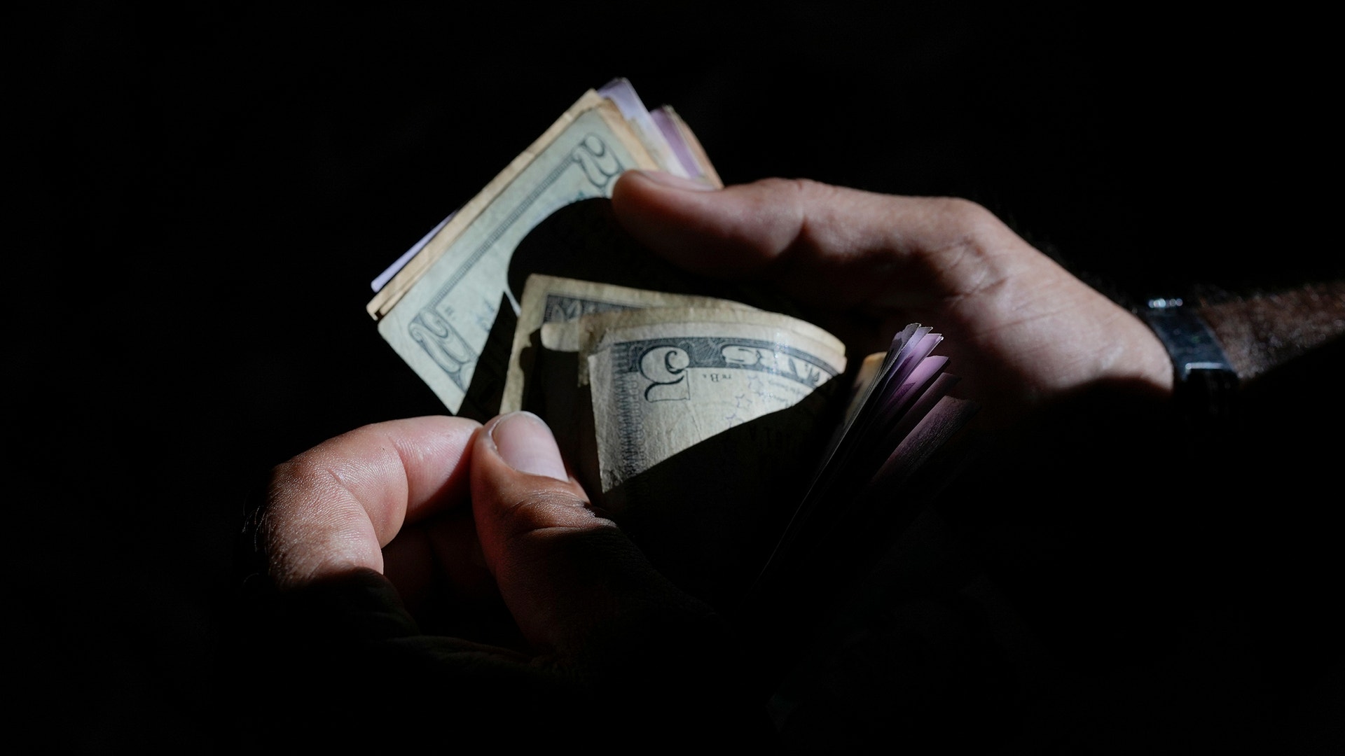 Händer som håller amerikanska dollarsedlar mot mörk bakgrund