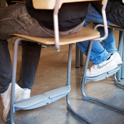 Elever sitter på stolar i ett klassrum, fotografi från lågt perspektiv som visar deras fötter och ben.