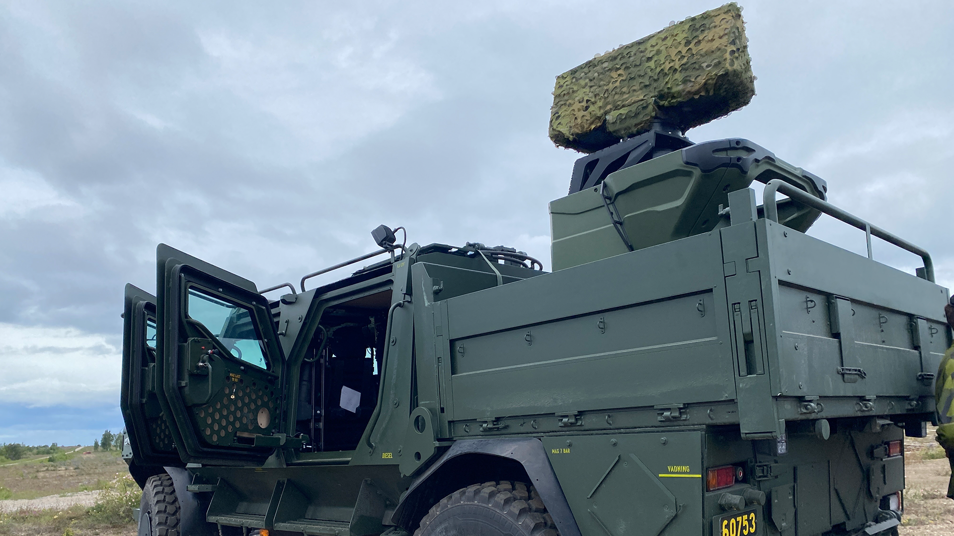 Militär lastbil i olivgrön färg med stor radarantenn monterad på taket, fotograferad i ett öppet landskap.
